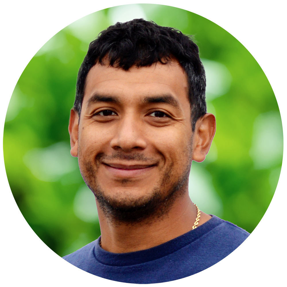 Close-up of a man smiling outdoors with a blurred green background.