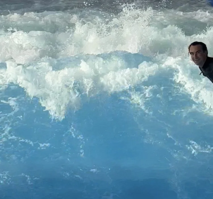 Ein Mann steht inmitten von sprudelndem Wasser, vermutlich in einem Fluss oder Meer, und lächelt in die Kamera.