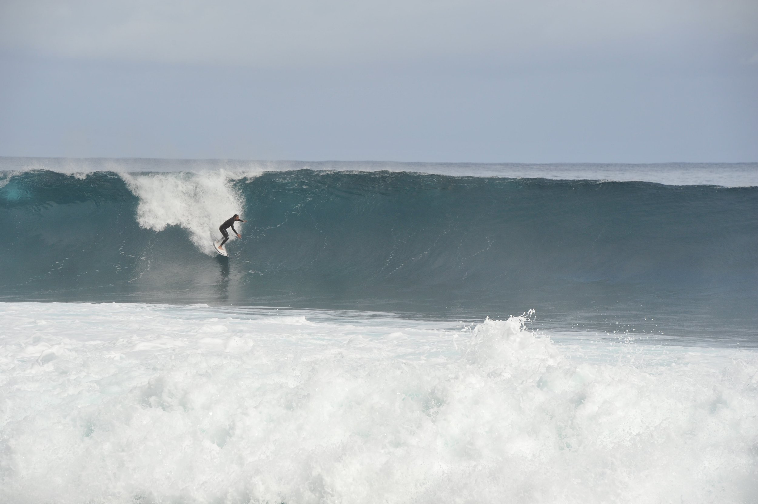 Eine Bombe die gegen einen Strand im Atlantik haut - ein Surfer der sich nach erfolgreichem Take-off bereit macht die Tube zu surfen