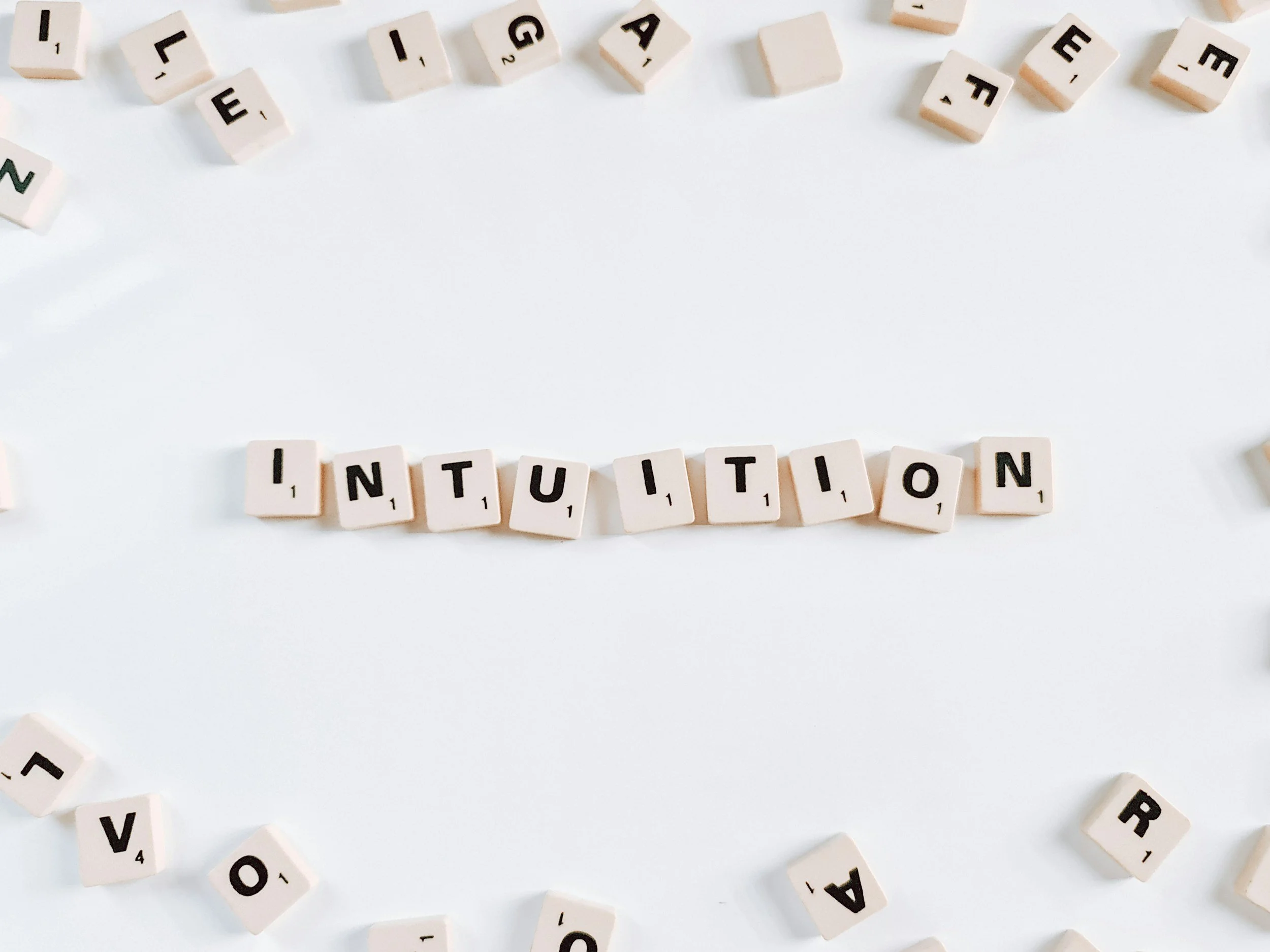 Scrabble tiles spelling 'INTUITION' on a white surface with scattered tiles around.