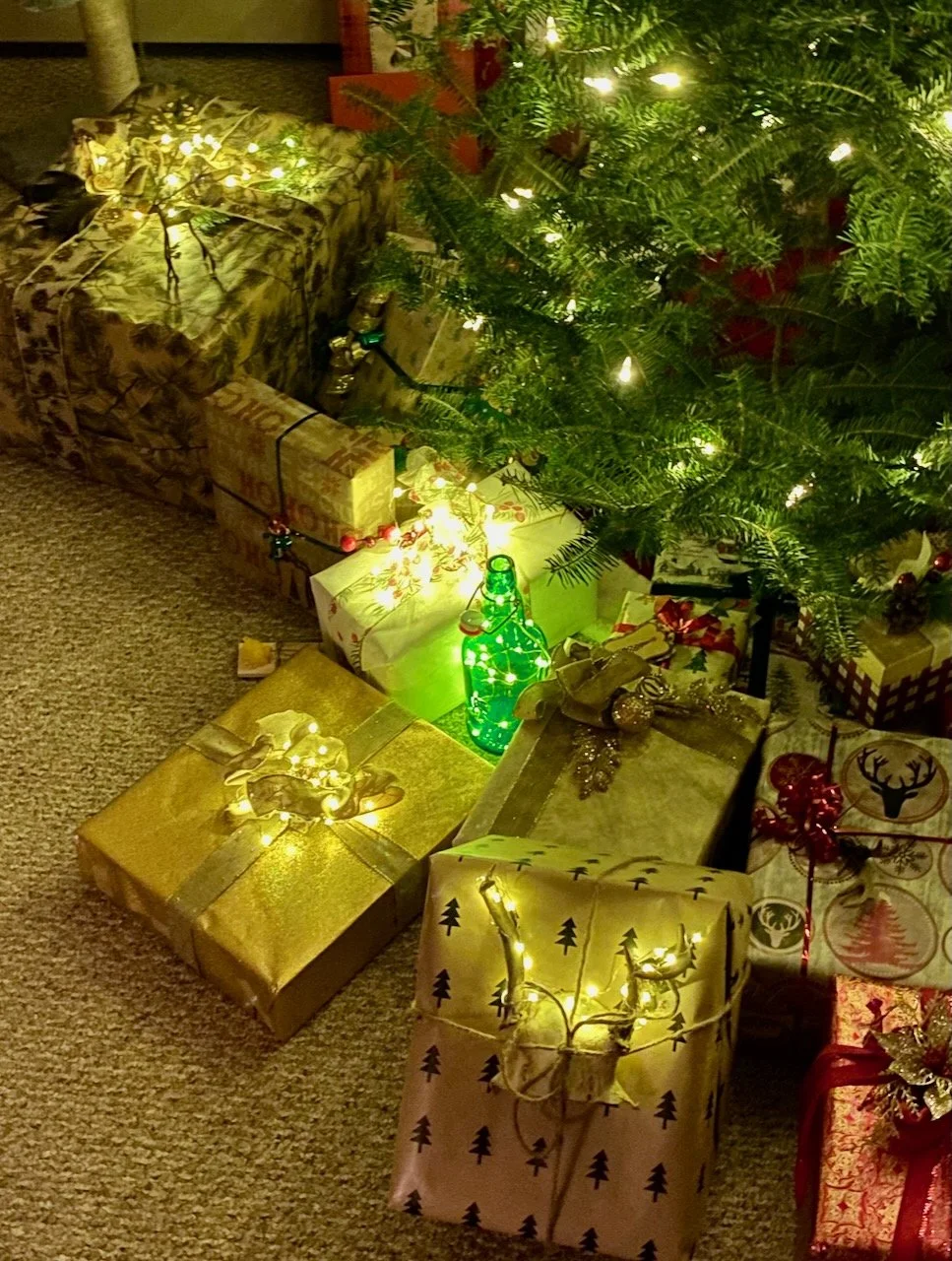 Christmas tree with lights surrounded by wrapped presents and decorations on a carpeted floor.
