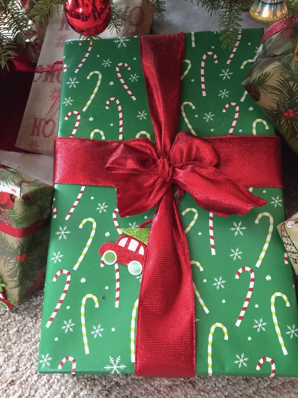 Green Christmas gift wrap decorated with candy canes and snowflakes, wrapped with a shiny red bow.