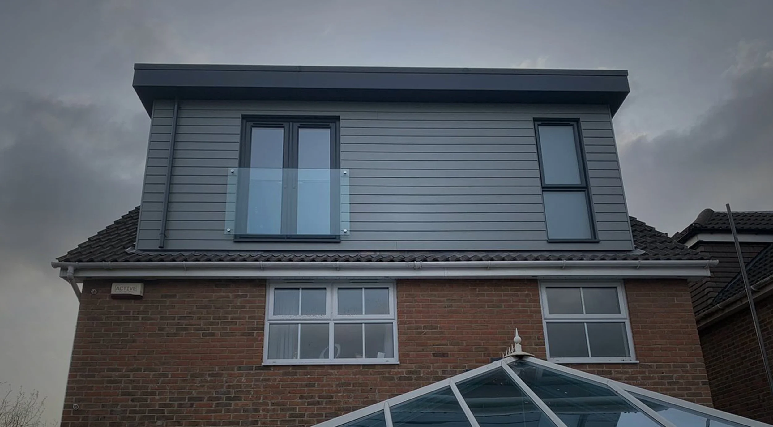 A large dormer loft conversion, a glass-paneled balcony, and windows, against a cloudy sky.