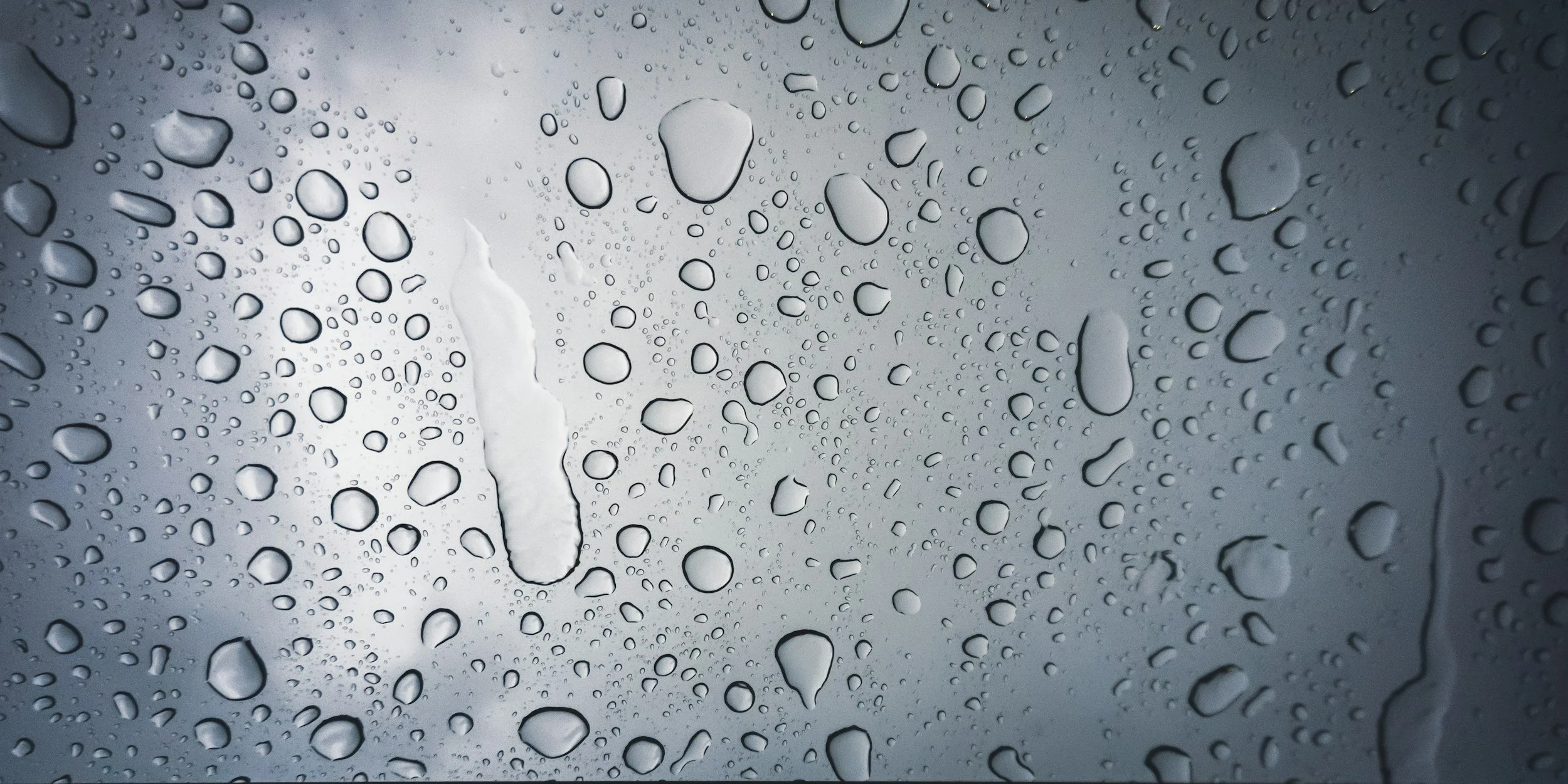 Close-up of a glass surface with water droplets and streaks, suggesting it is raining.