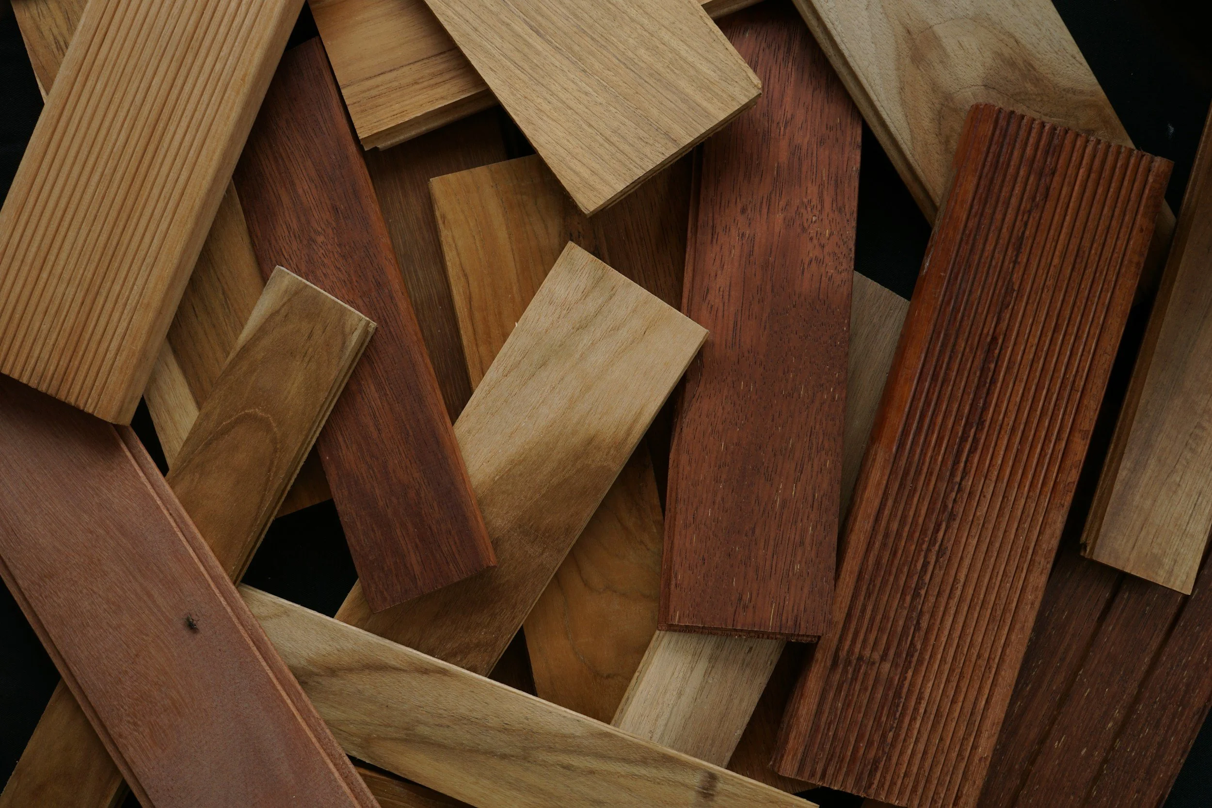A collection of various wooden planks with different shades and grain patterns, arranged loosely.
