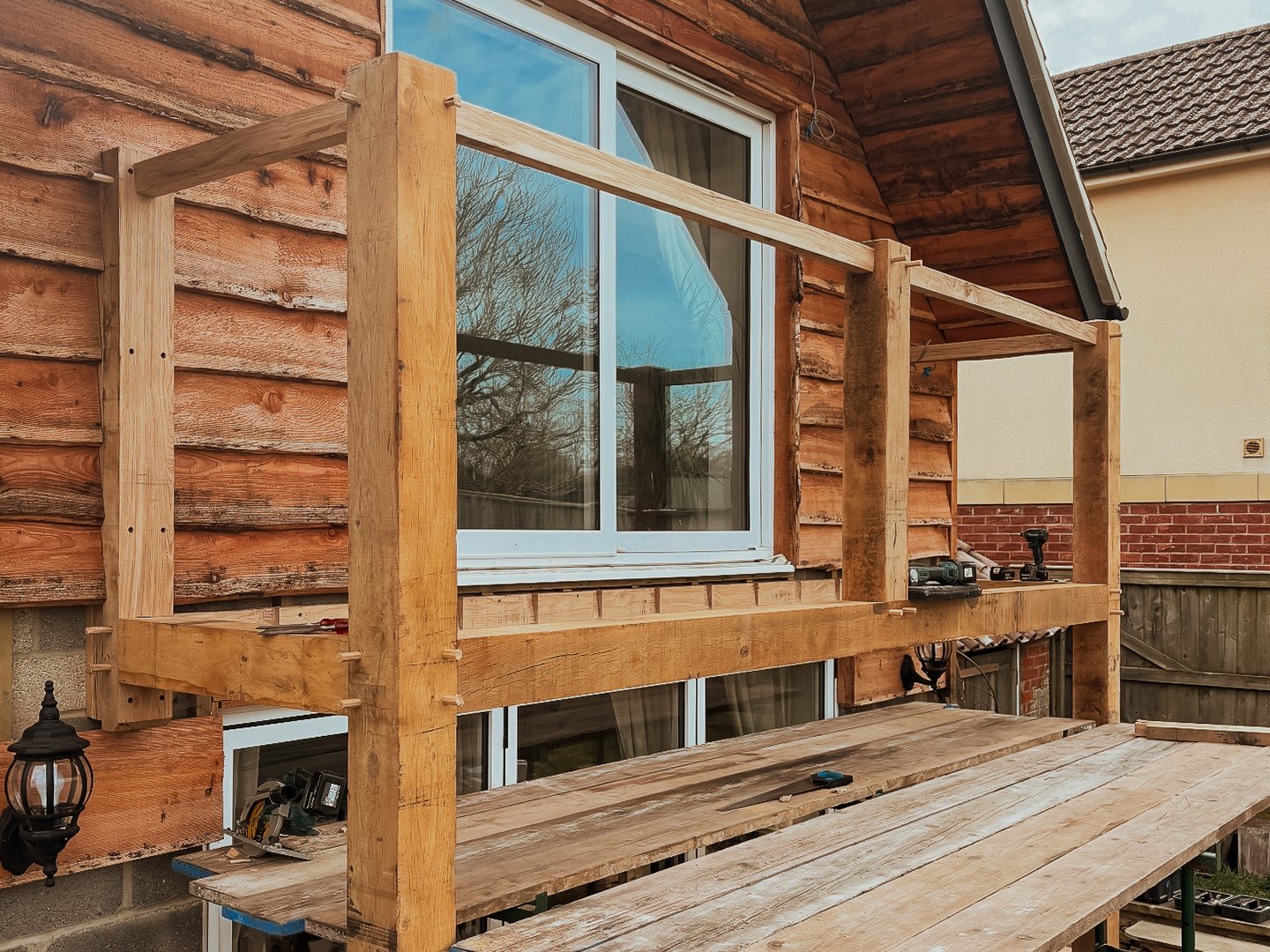 Wooden balcony railing under construction on a house with a brick and wood exterior.