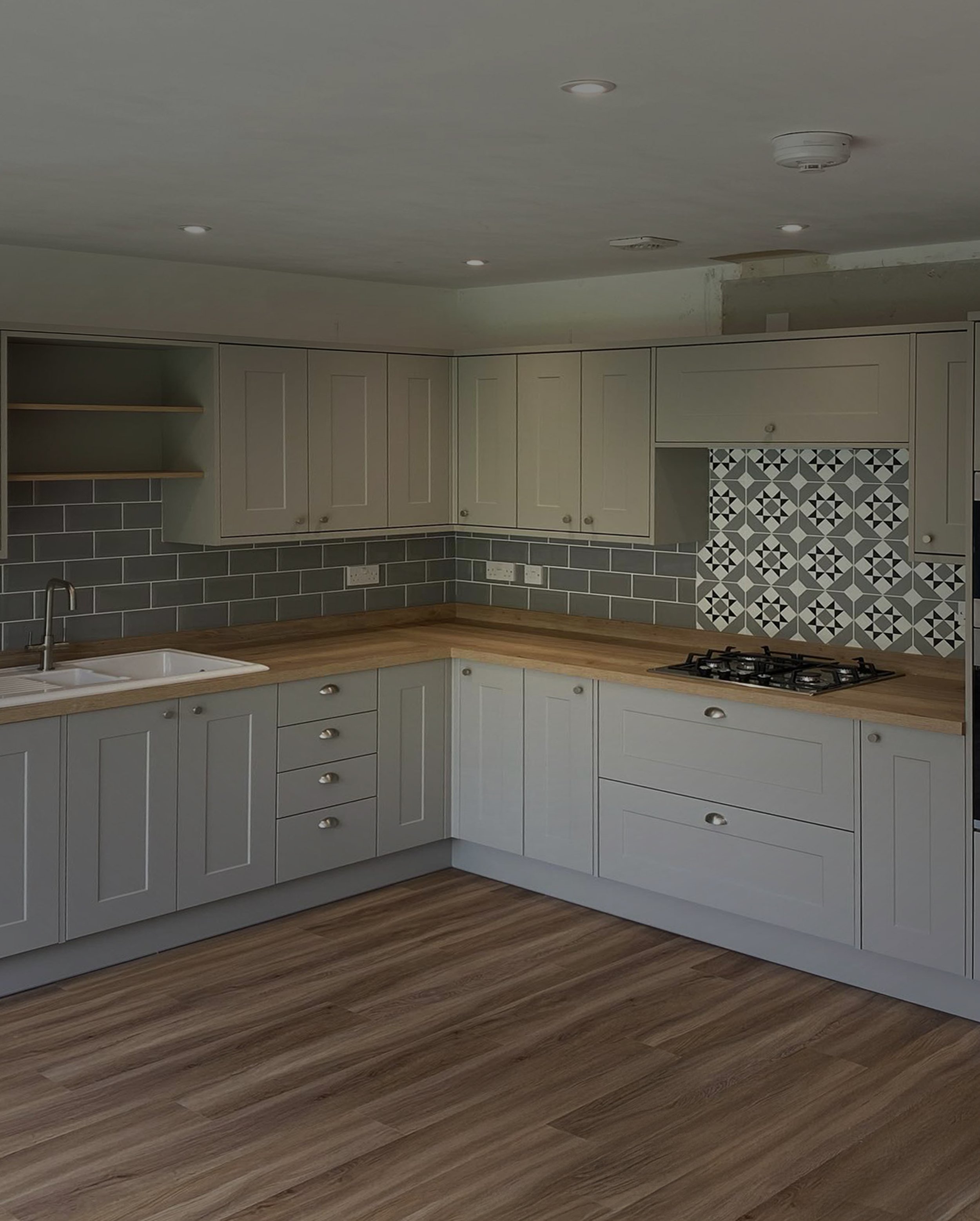 Modern L-shaped kitchen with light gray cabinets, wood countertops, patterned tile backsplash, and wooden plank flooring.