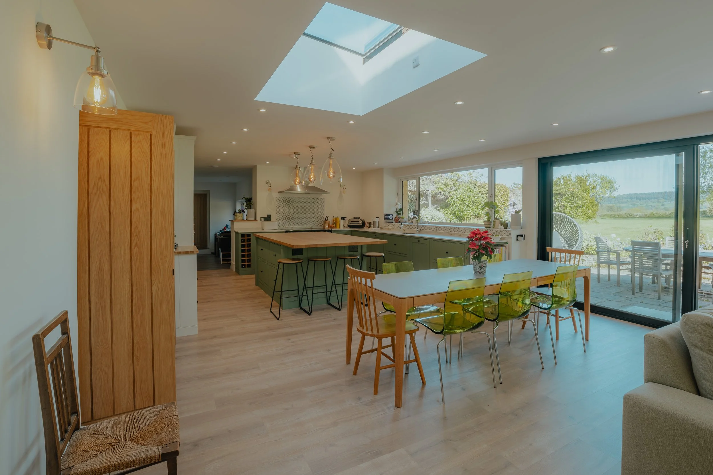 Open-concept kitchen and dining area with large sliding glass doors leading to an outdoor patio, a skylight, and modern light fixtures.