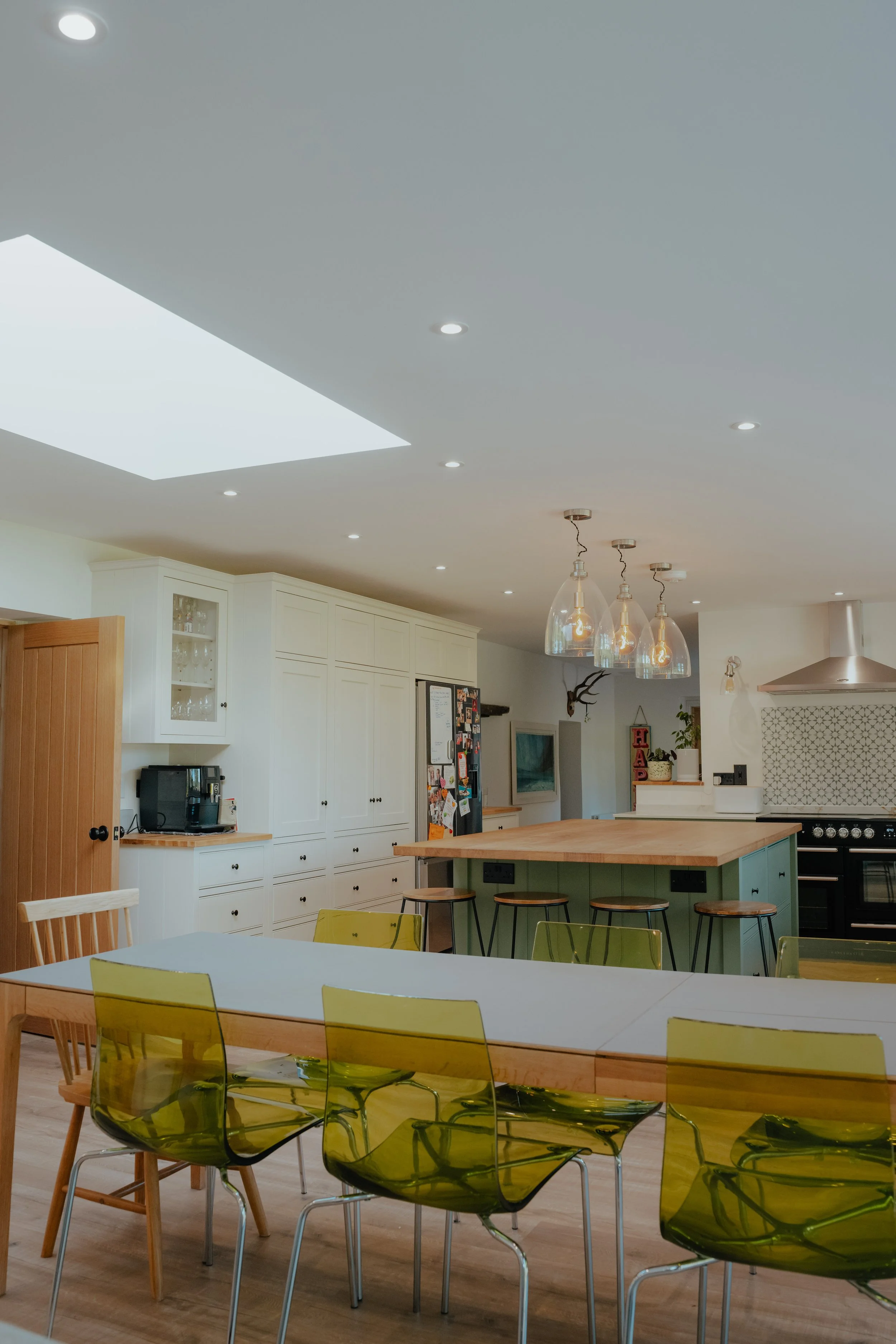 Modern kitchen with white cabinets, a wooden kitchen island with green base, pendant lights, and a dining table with yellow chairs.