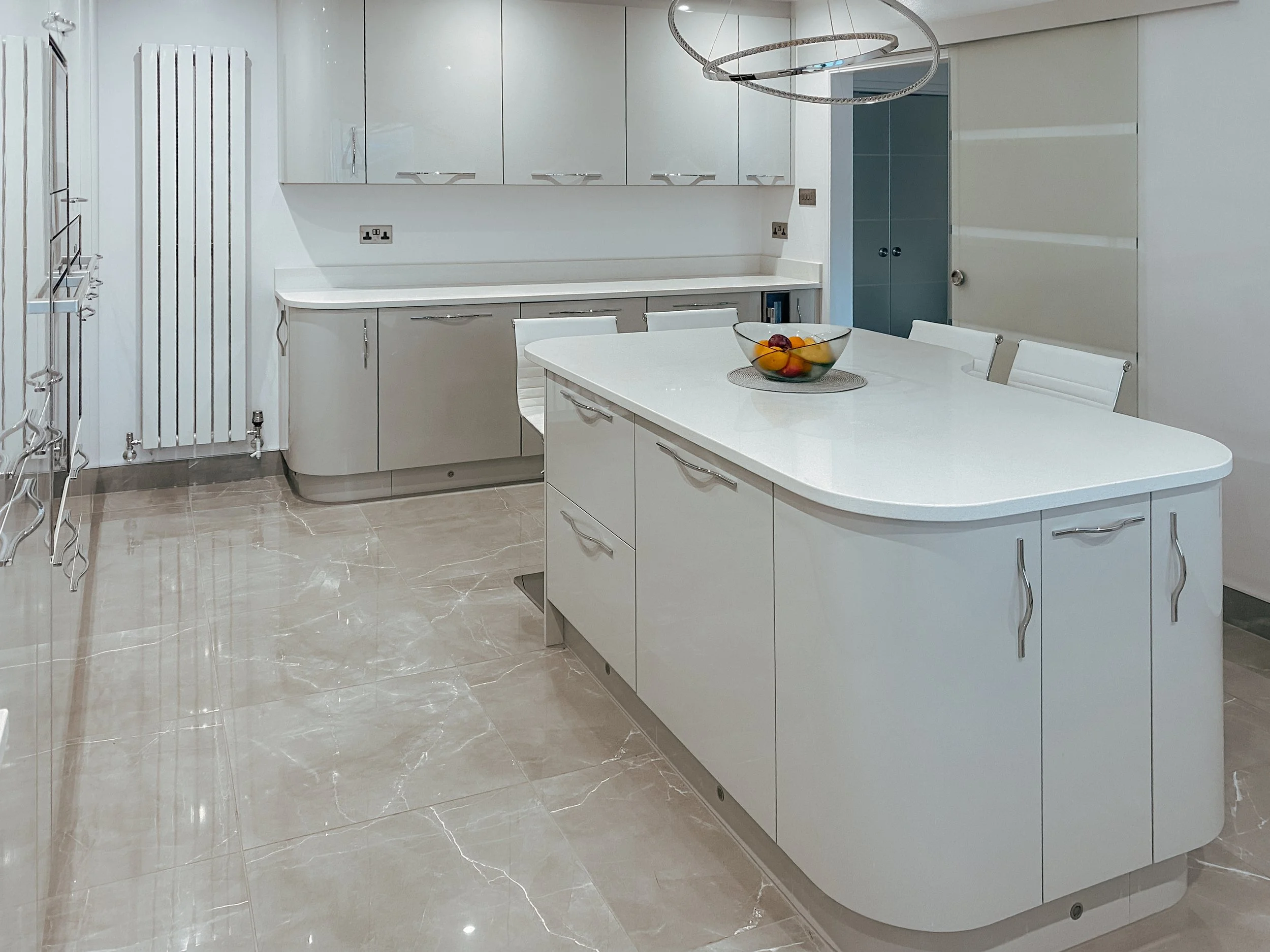Modern white kitchen with an island, placed bowl of fruit, and white cabinets.