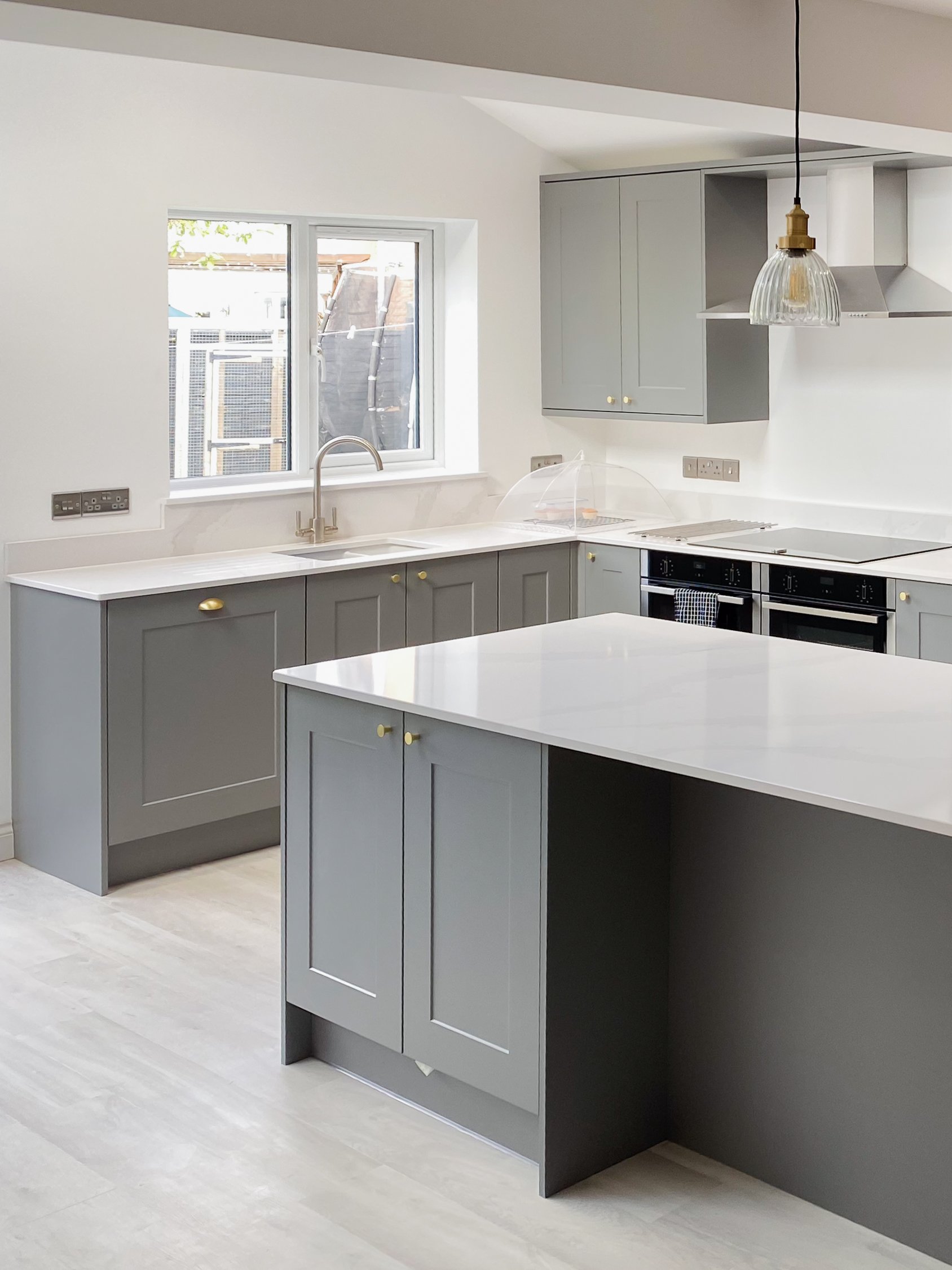 Modern kitchen with gray cabinets, white countertops, a window above the sink, and a hanging pendant light.