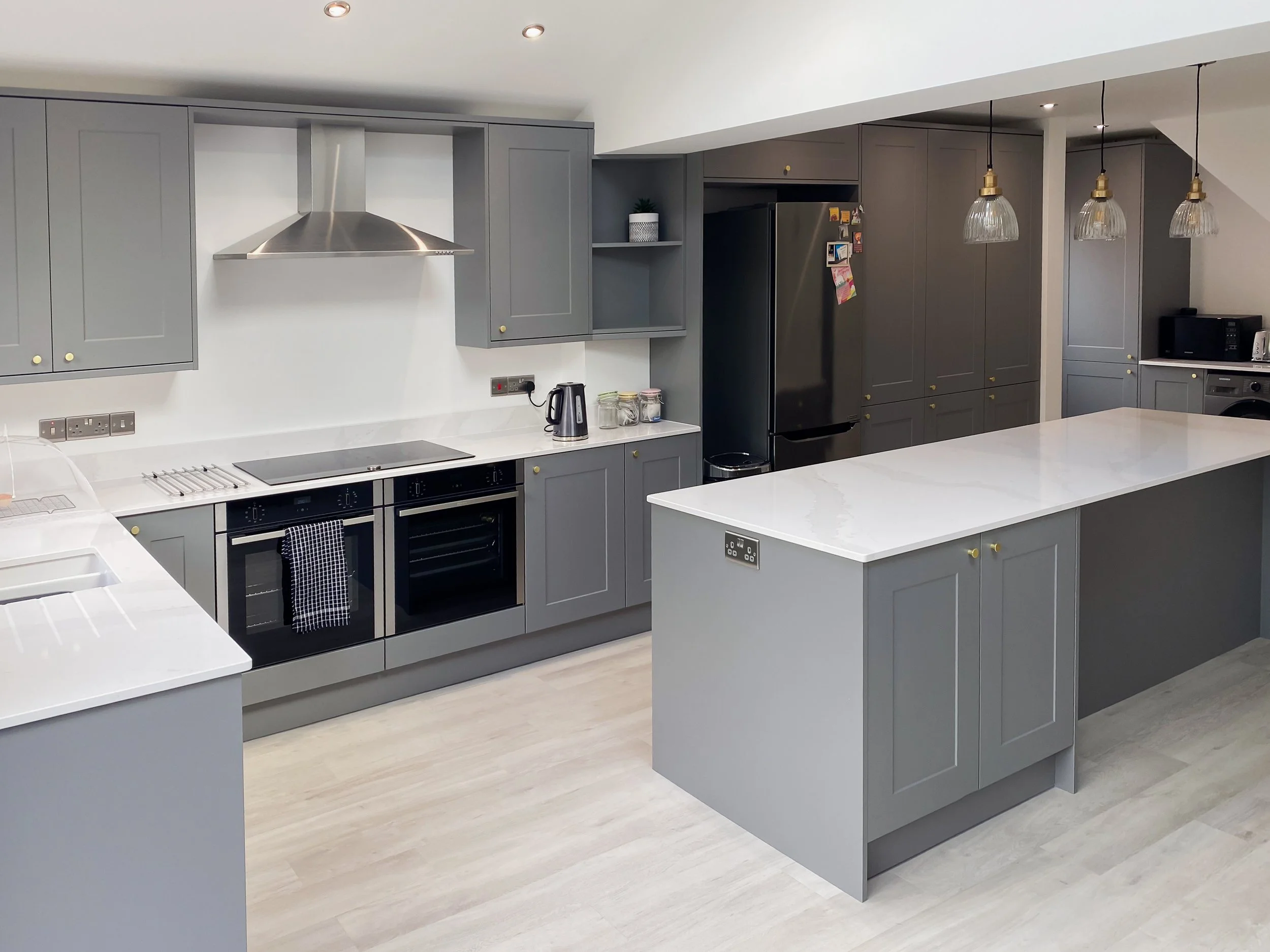 Modern kitchen with grey cabinets, white marble island, stainless steel appliances, pendant lights, and light hardwood flooring.