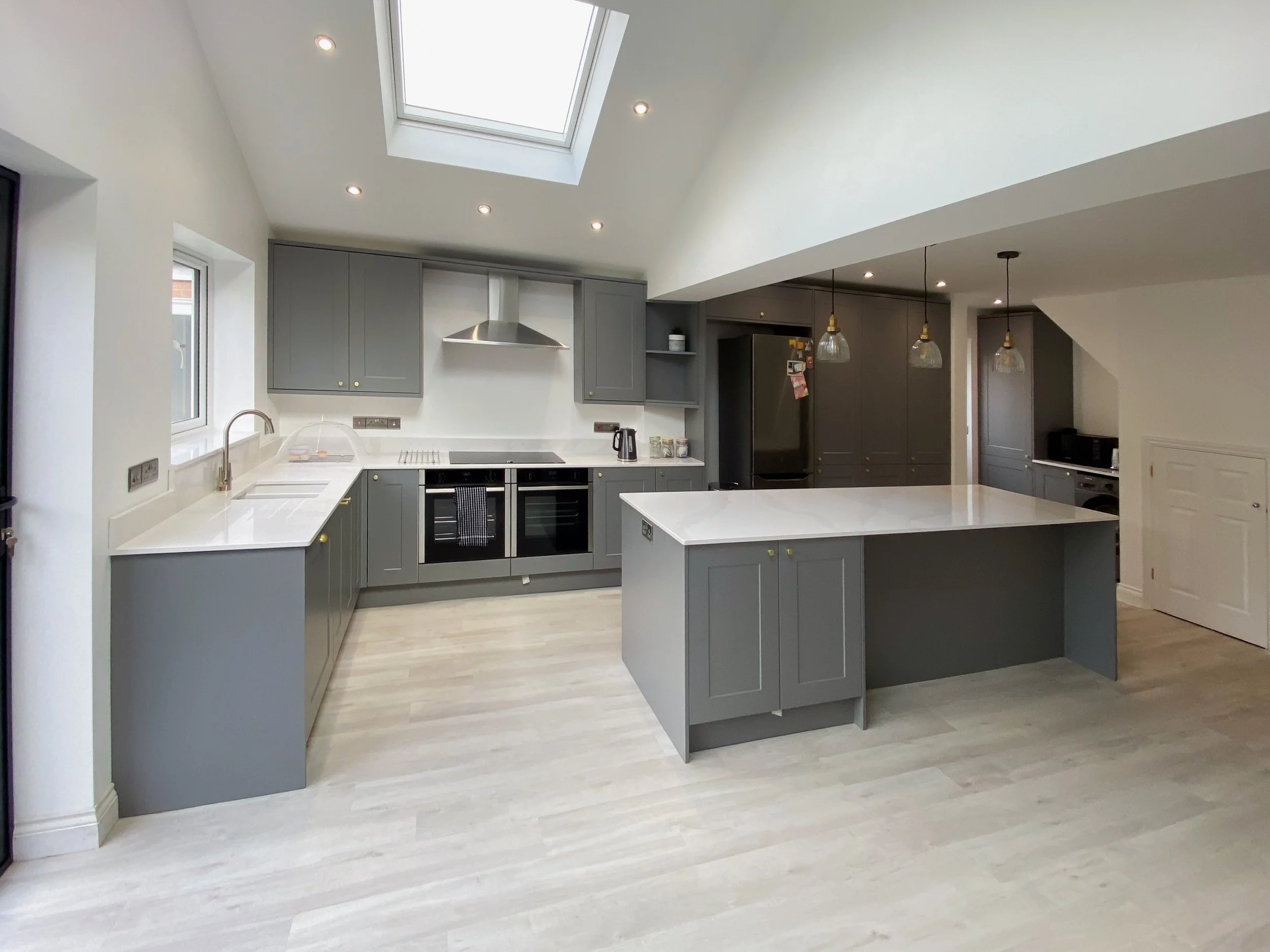Modern kitchen with gray cabinets, white countertops, a central island, a skylight, and pendant lighting