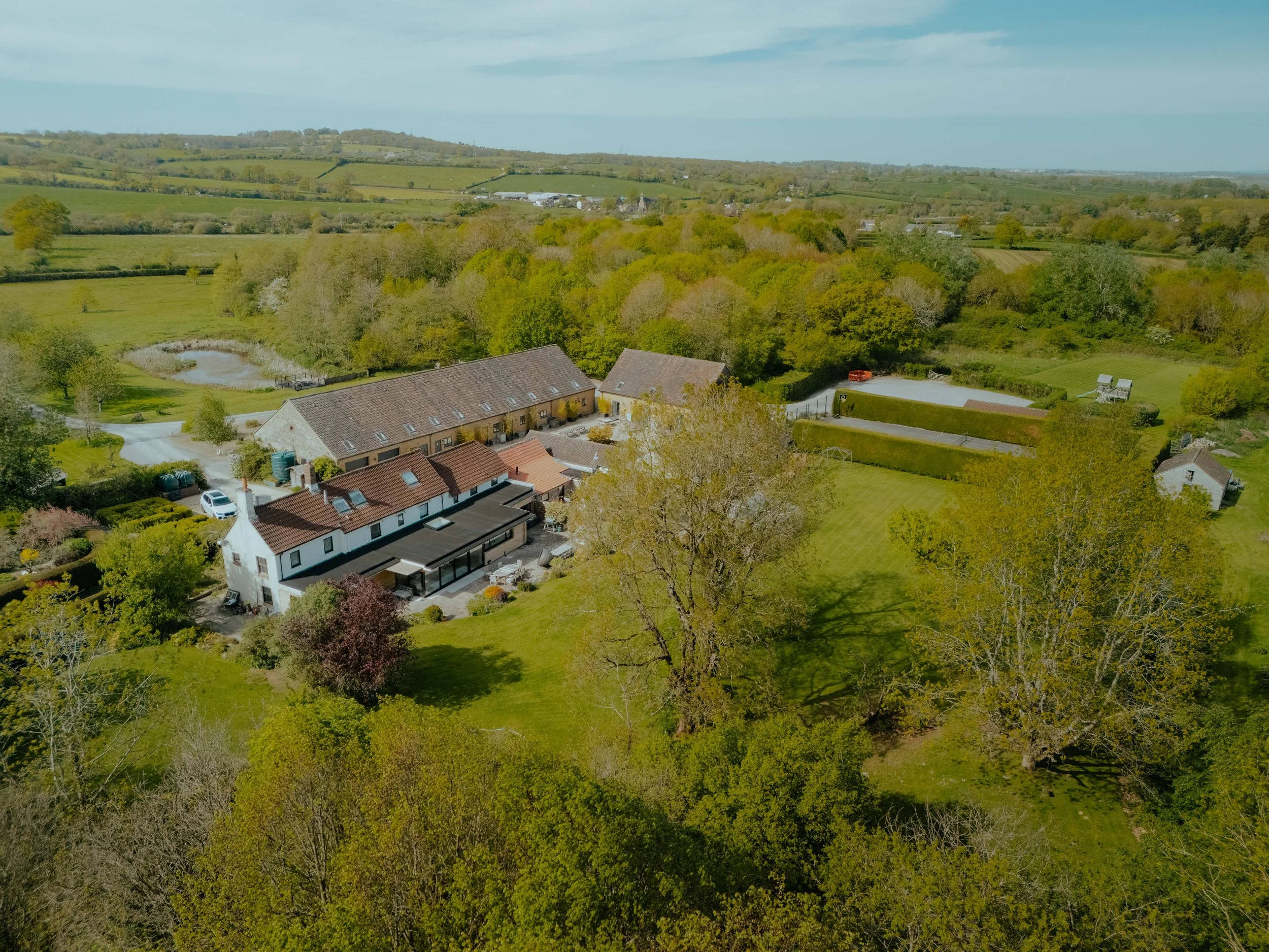 An aerial view of a rural landscape with houses, trees, and green fields under a partly cloudy sky. An aerial view of a contemporary home extension and renovation.