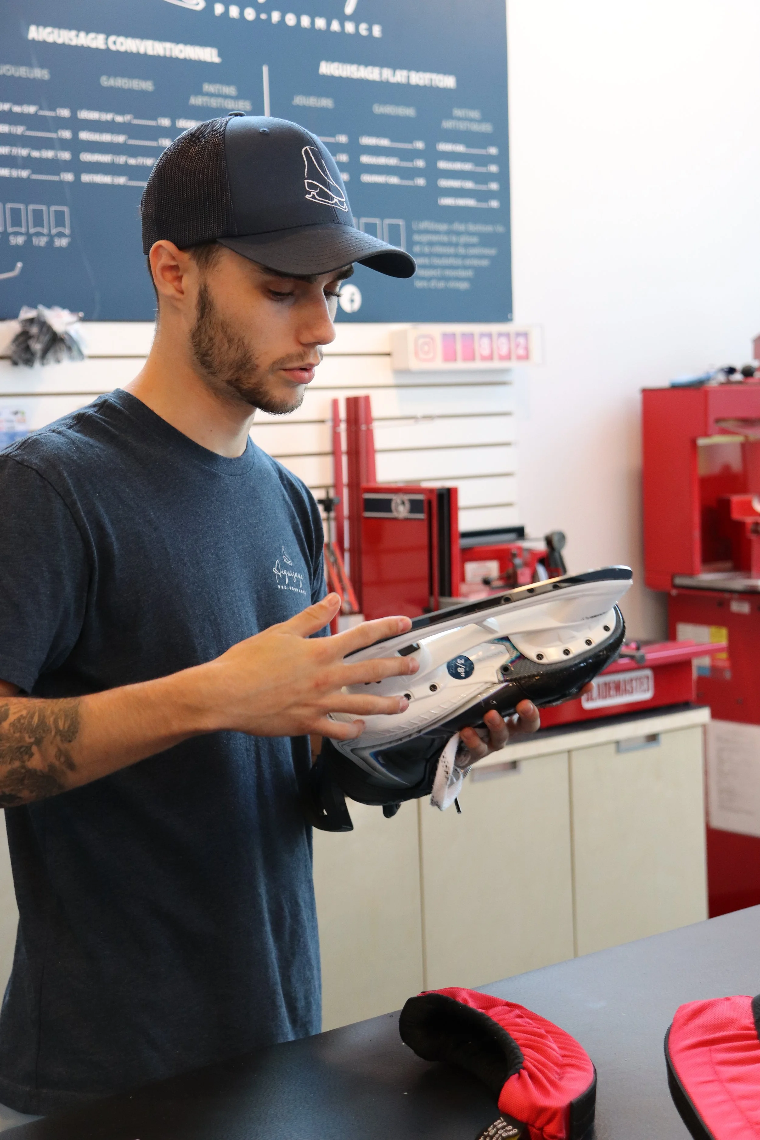 Jeune homme en magasin de sport, regardant une chaussure de ski. Arrière-plan avec tableau d'information et outils rouges.