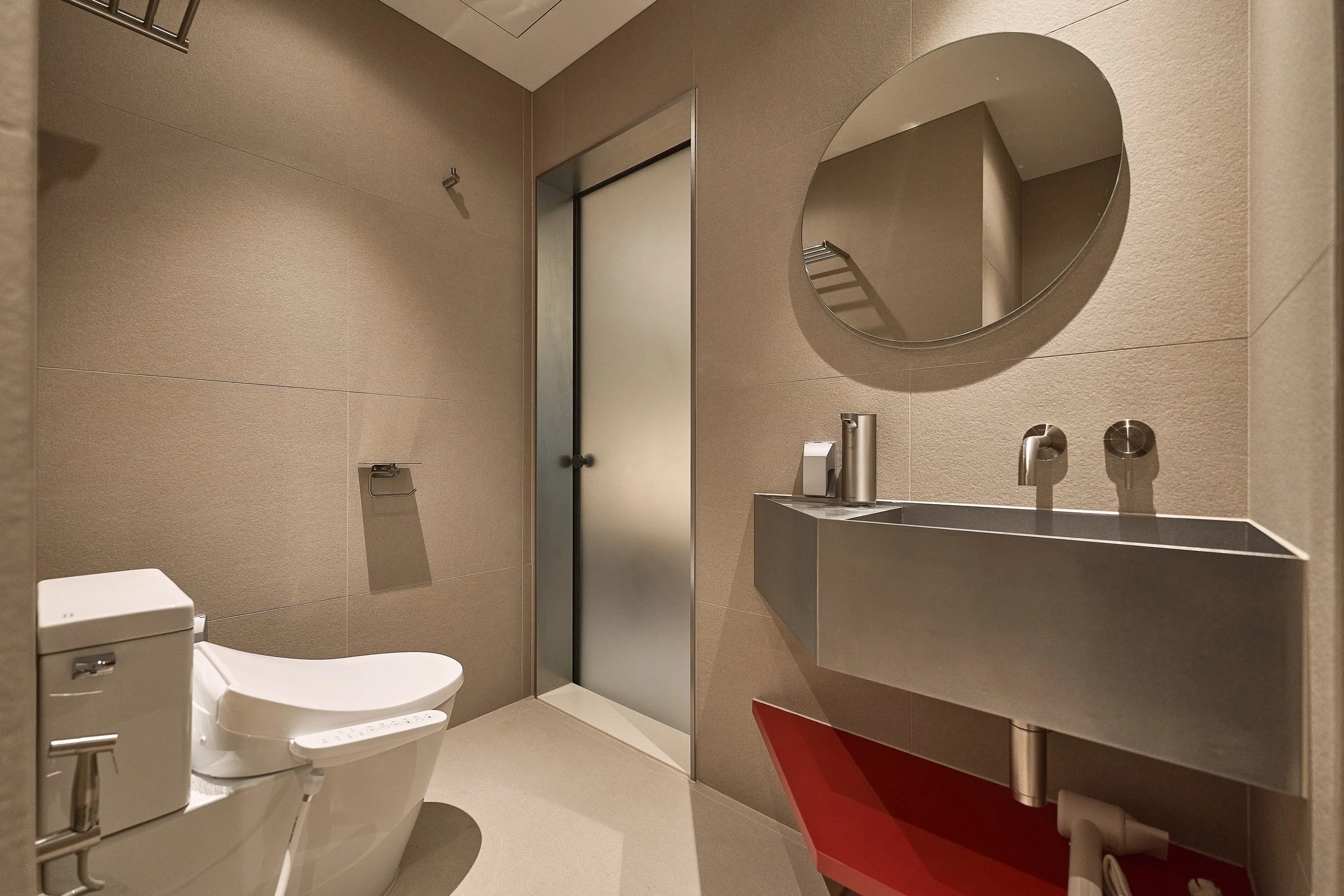 Modern bathroom in Willow Leaf Gangnam Room 201 featuring a bidet toilet, minimalist stainless-steel vanity, round mirror, and warm beige tiles.
