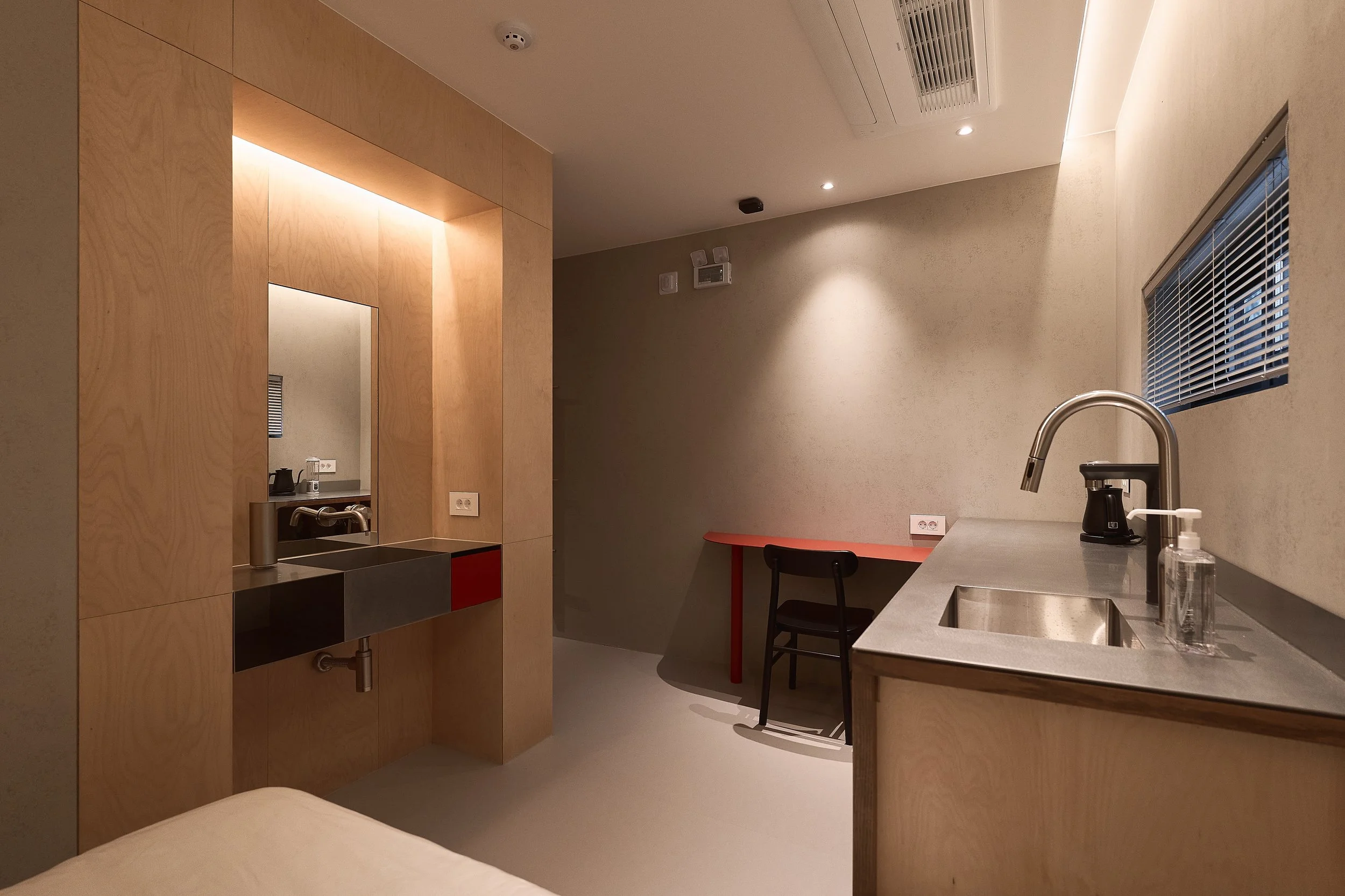 A modern willow leaf Gangnam studio room with a minimalist vanity, stainless-steel kitchenette, warm wood paneling, and a compact red desk for work or study.