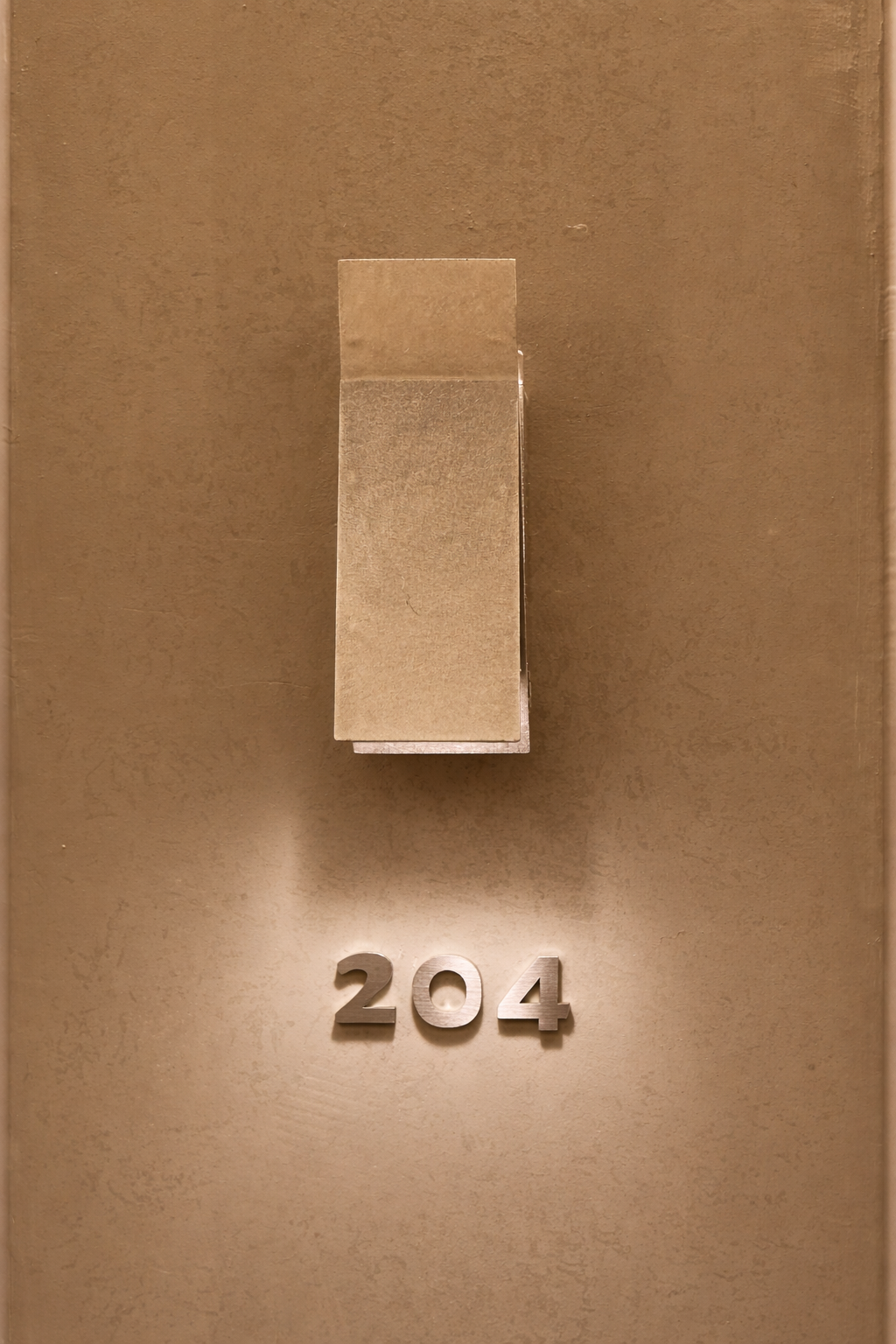 A warm-toned willow leaf stay Gangnam room door featuring a brushed-metal wall lamp illuminating the metallic room number 204 on a textured beige wall.