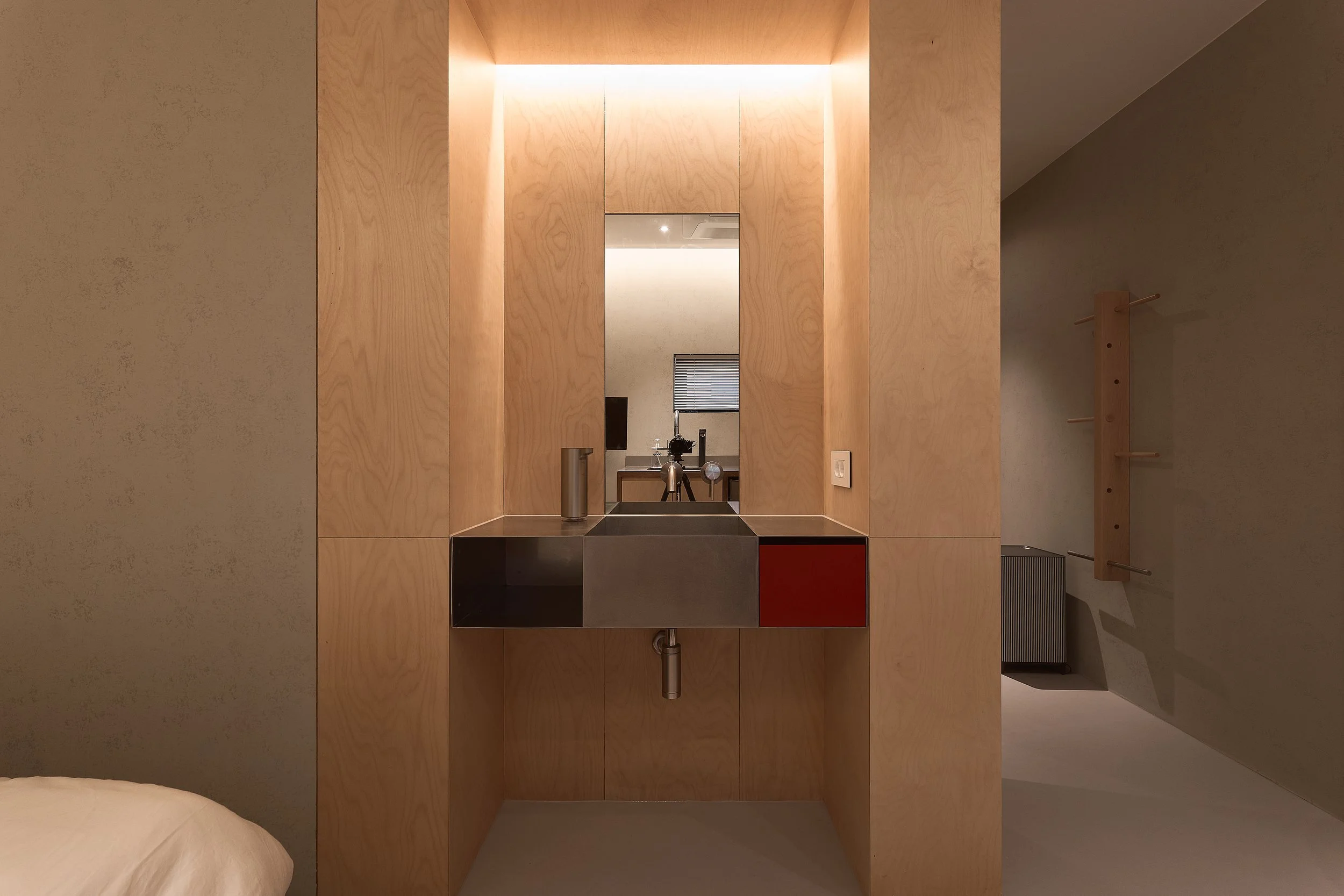 A minimalist vanity area in a willow leaf Gangnam room, featuring a stainless-steel sink, warm wood paneling, soft indirect lighting, and a modern built-in mirror.