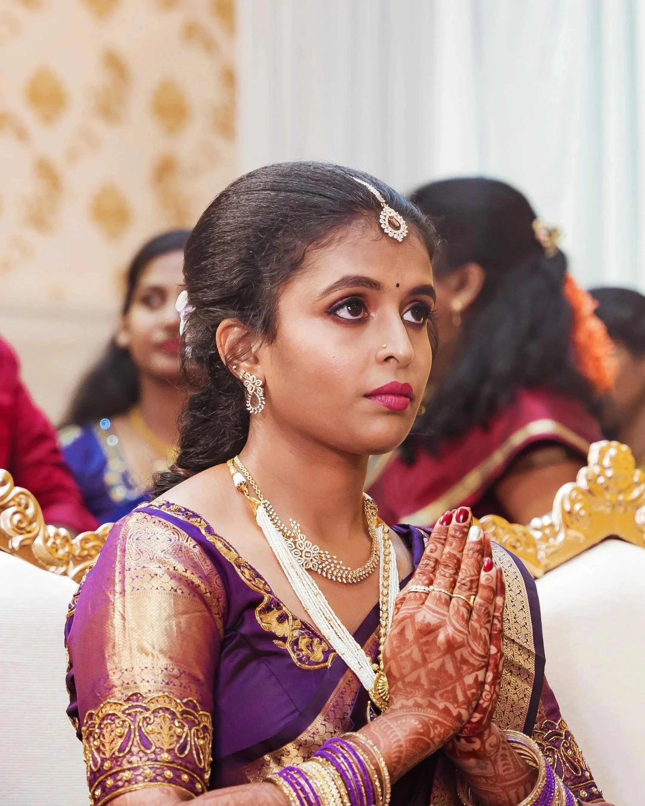 A woman dressed in traditional Indian attire, with jewelry and henna on her hands, during a ceremony.