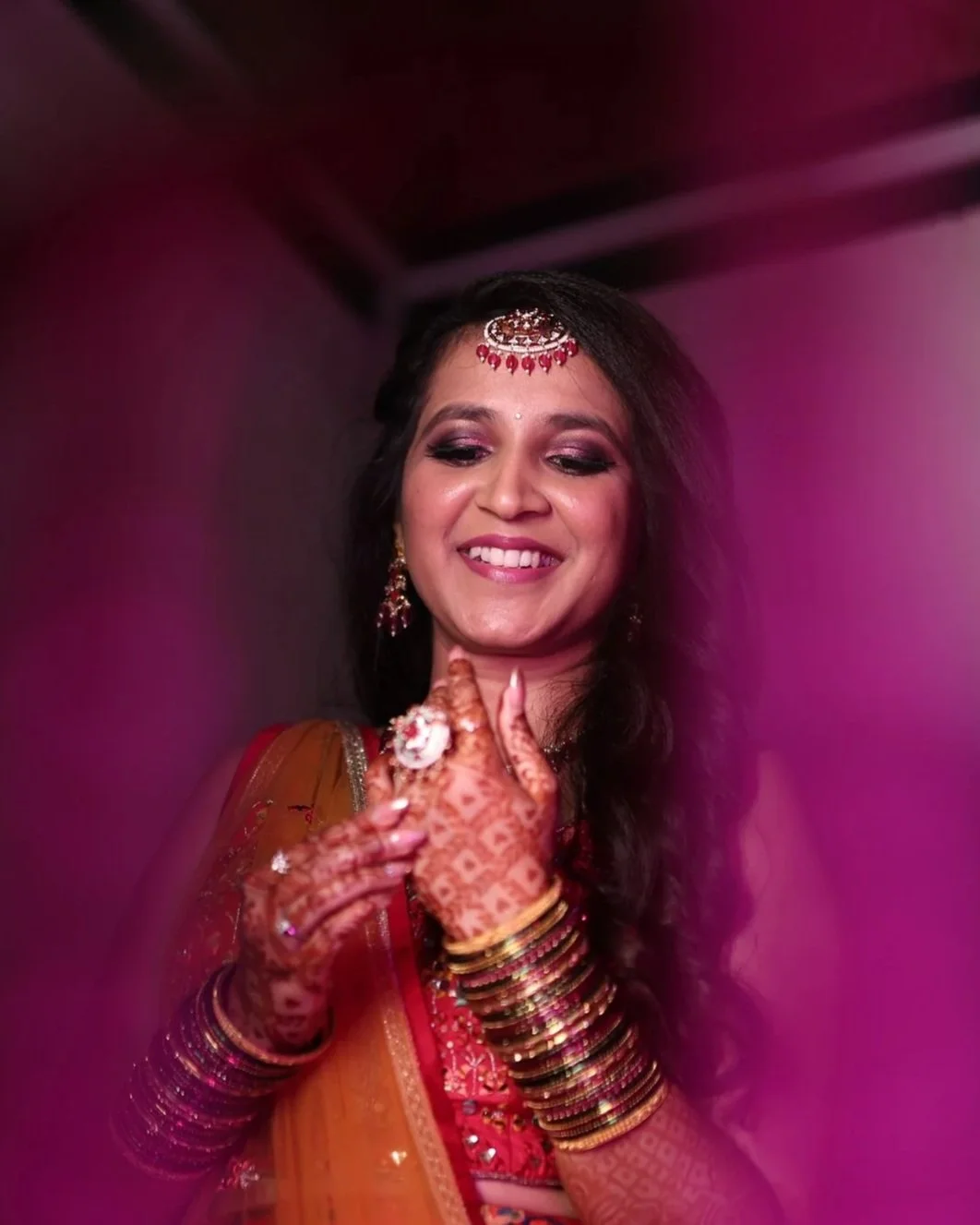 A woman with henna tattoos on her hands, dressed in traditional Indian attire, smiling and showing a gesture of joy.