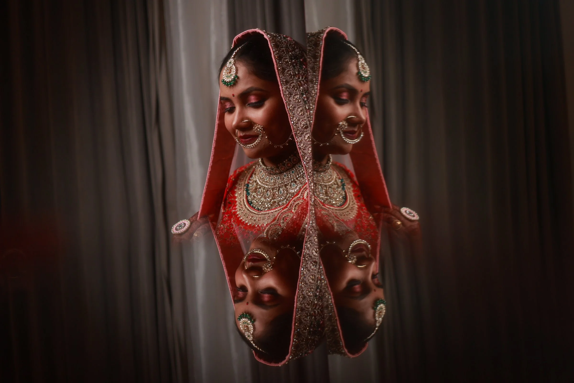 A woman dressed in traditional Indian bridal attire with intricate jewelry, reflected in a mirror