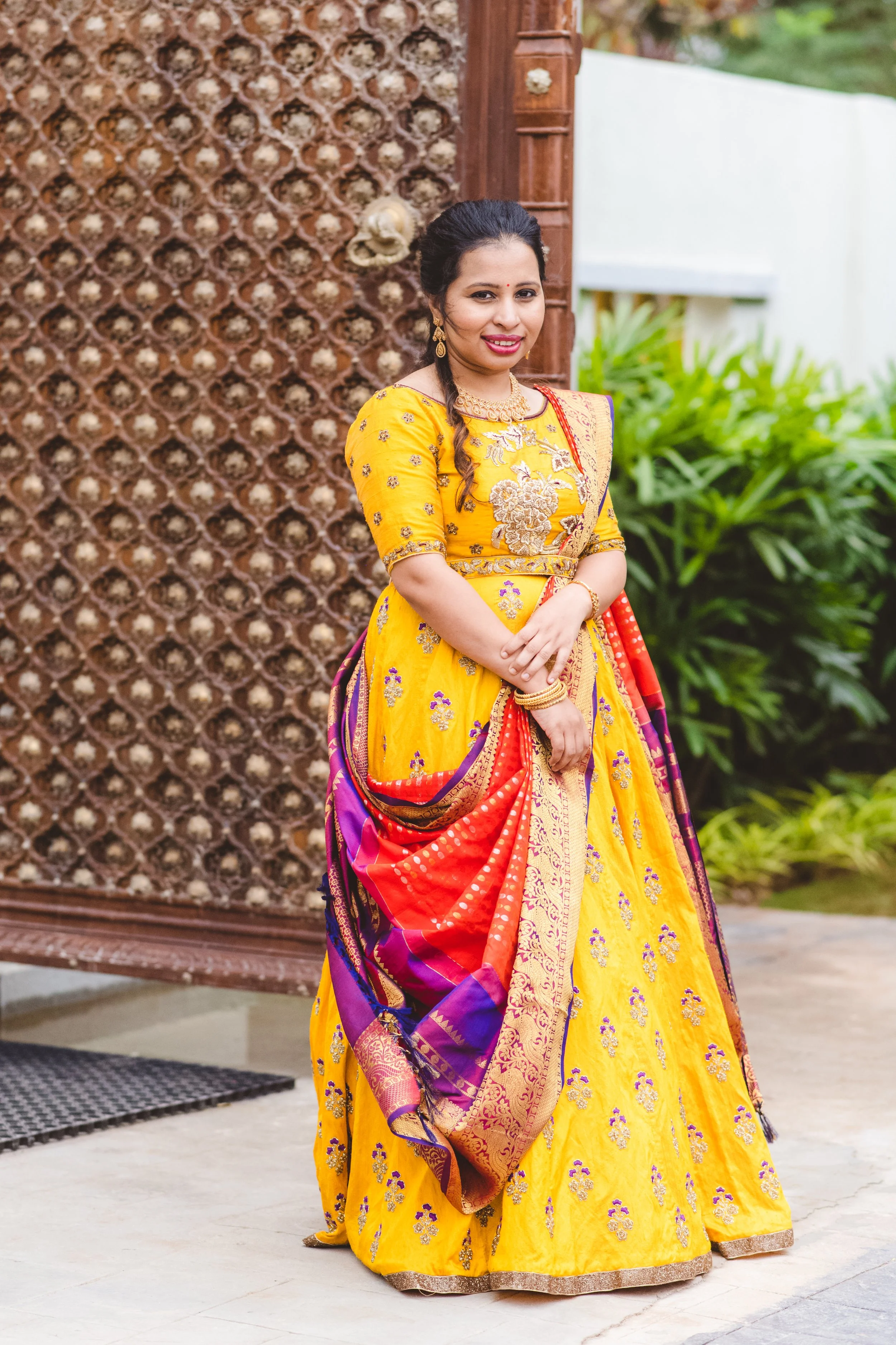 Woman in traditional yellow and multicolored dress smiling outdoors.