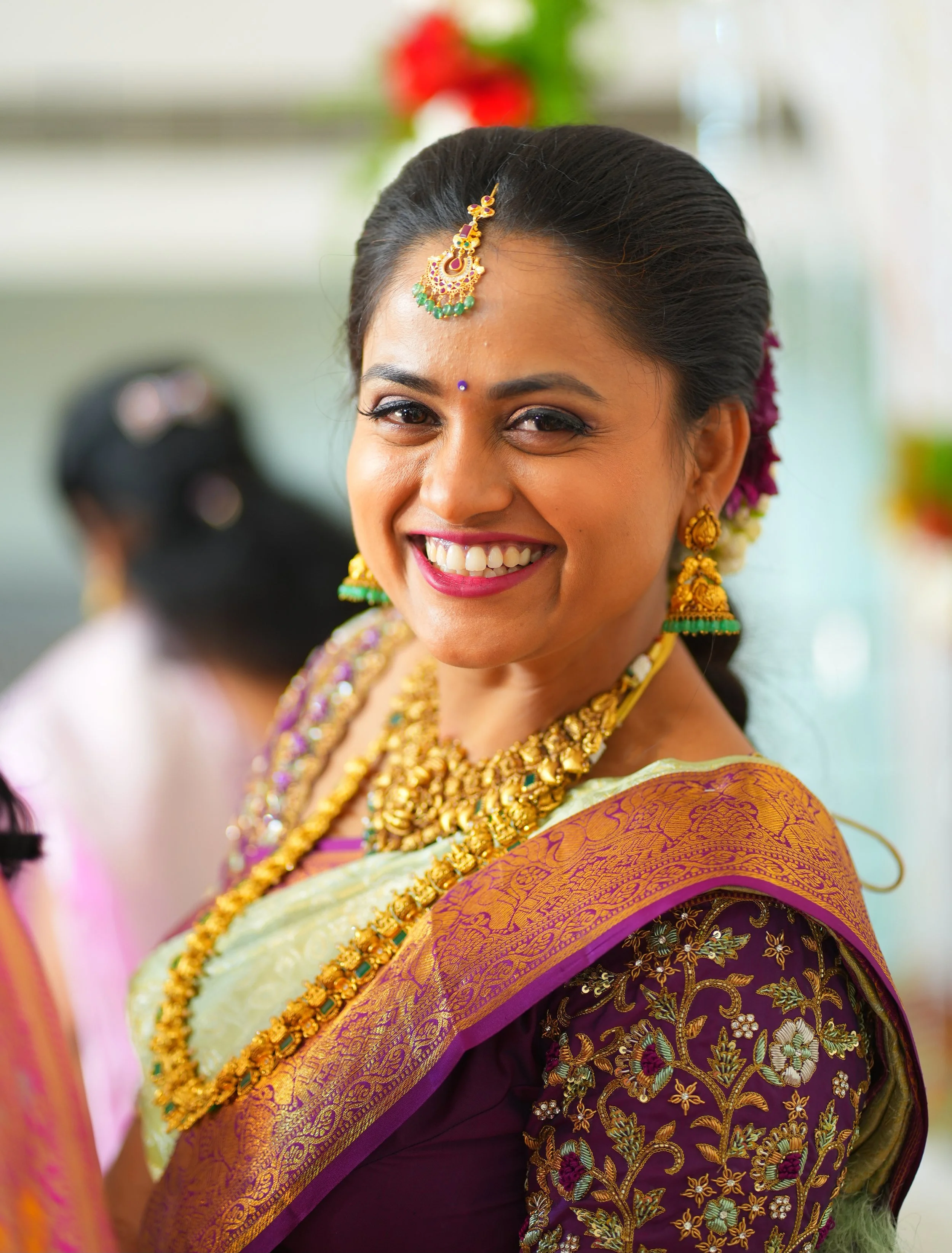 A woman wearing traditional Indian jewelry and clothing, smiling at the camera.