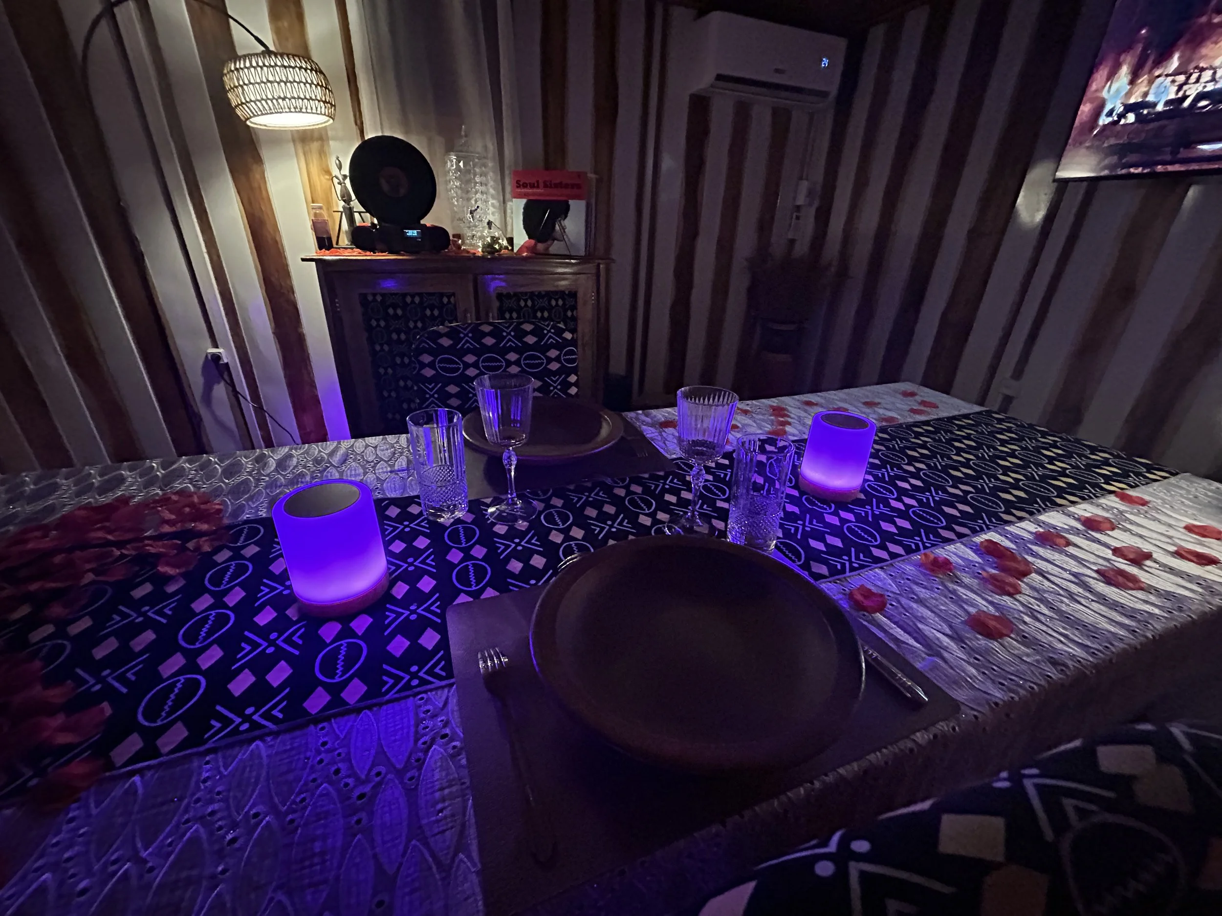 Table de dîner élégante et romantique dressée avec des verres, des assiettes et des bougies violettes dans une ambiance tamisée.