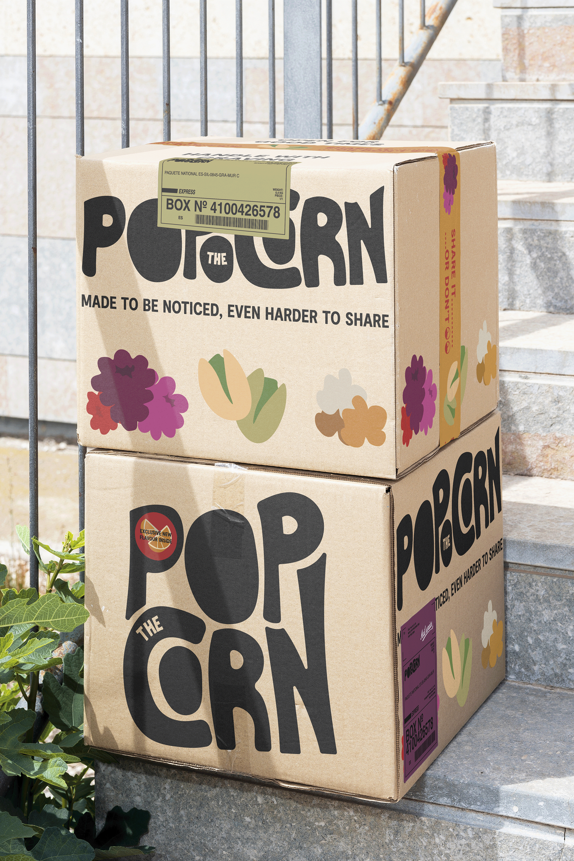 Two cardboard boxes labeled "Popcorn" stacked on outdoor stone stairs, with flower illustrations on the boxes and a green shipment sticker on the top box.