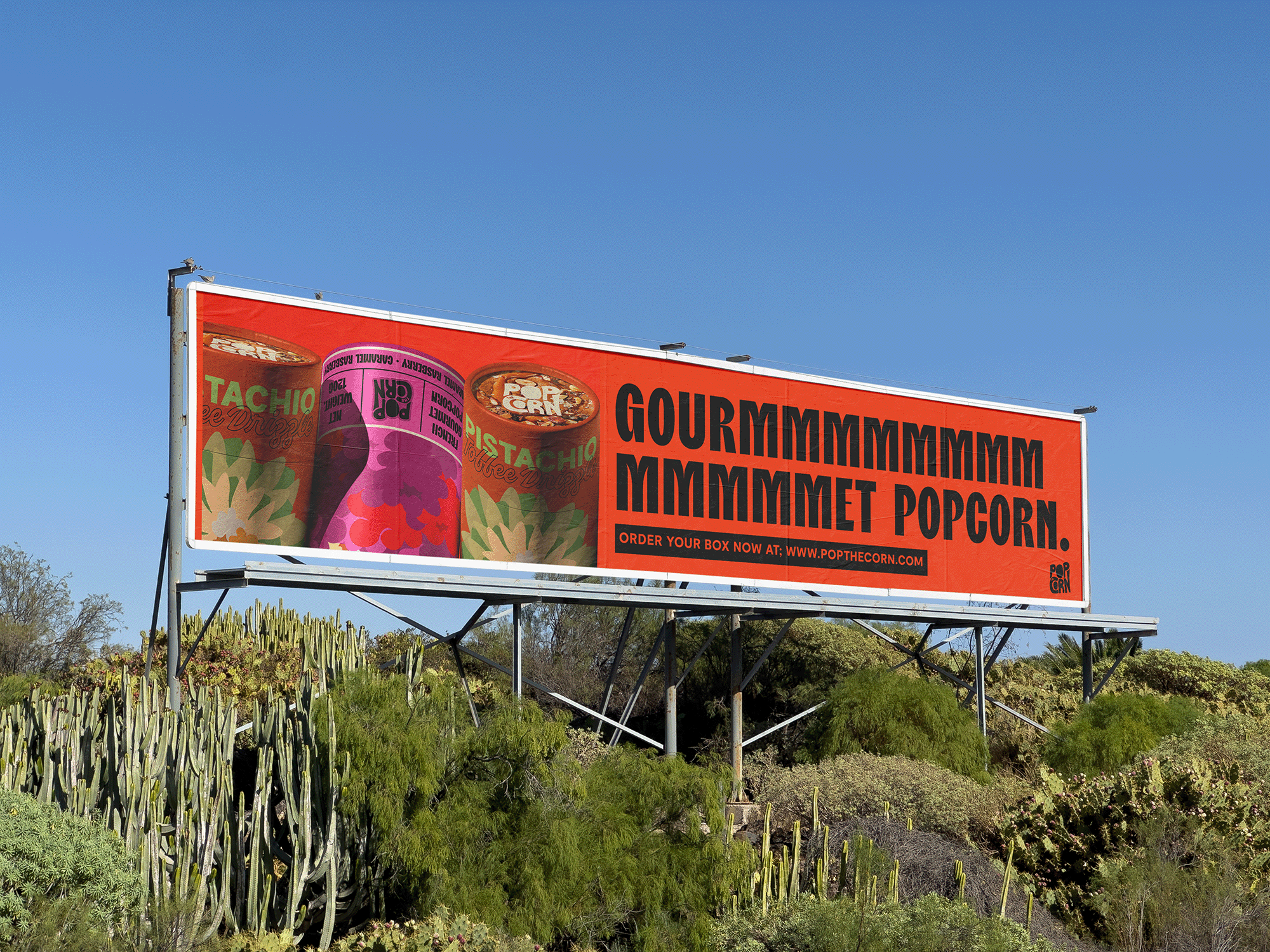 Billboard advertising popcorn with a purple and a green container of popcorn, with large black text reading "GOURMMMMMMMMMMMMMMMMM POPCORN" and a call to action website link at the bottom. Abubakr Design Co Brand Identity Designer from East London