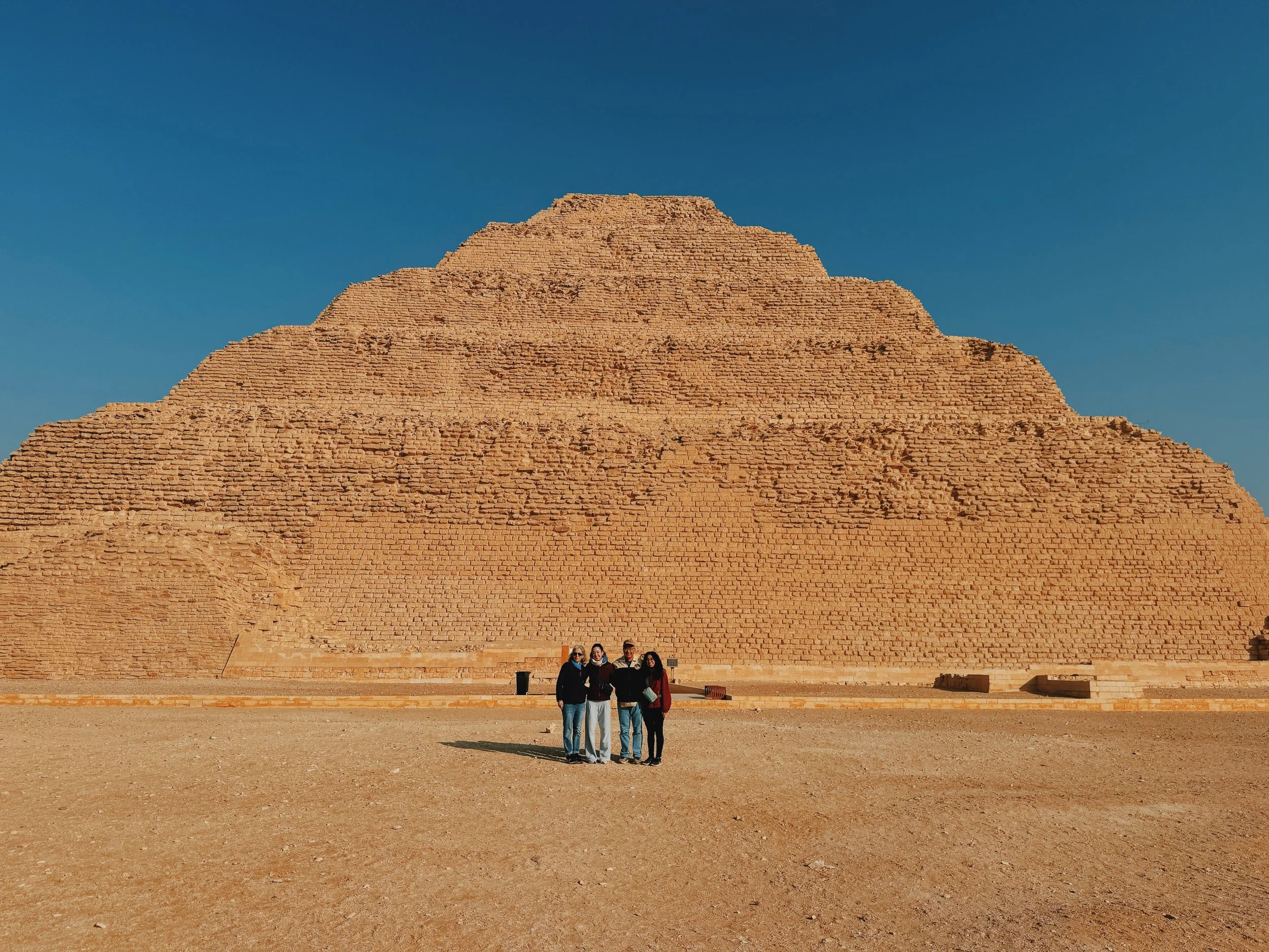 Travelers standing before the Step Pyramid of Djoser at Saqqara under a clear blue sky.