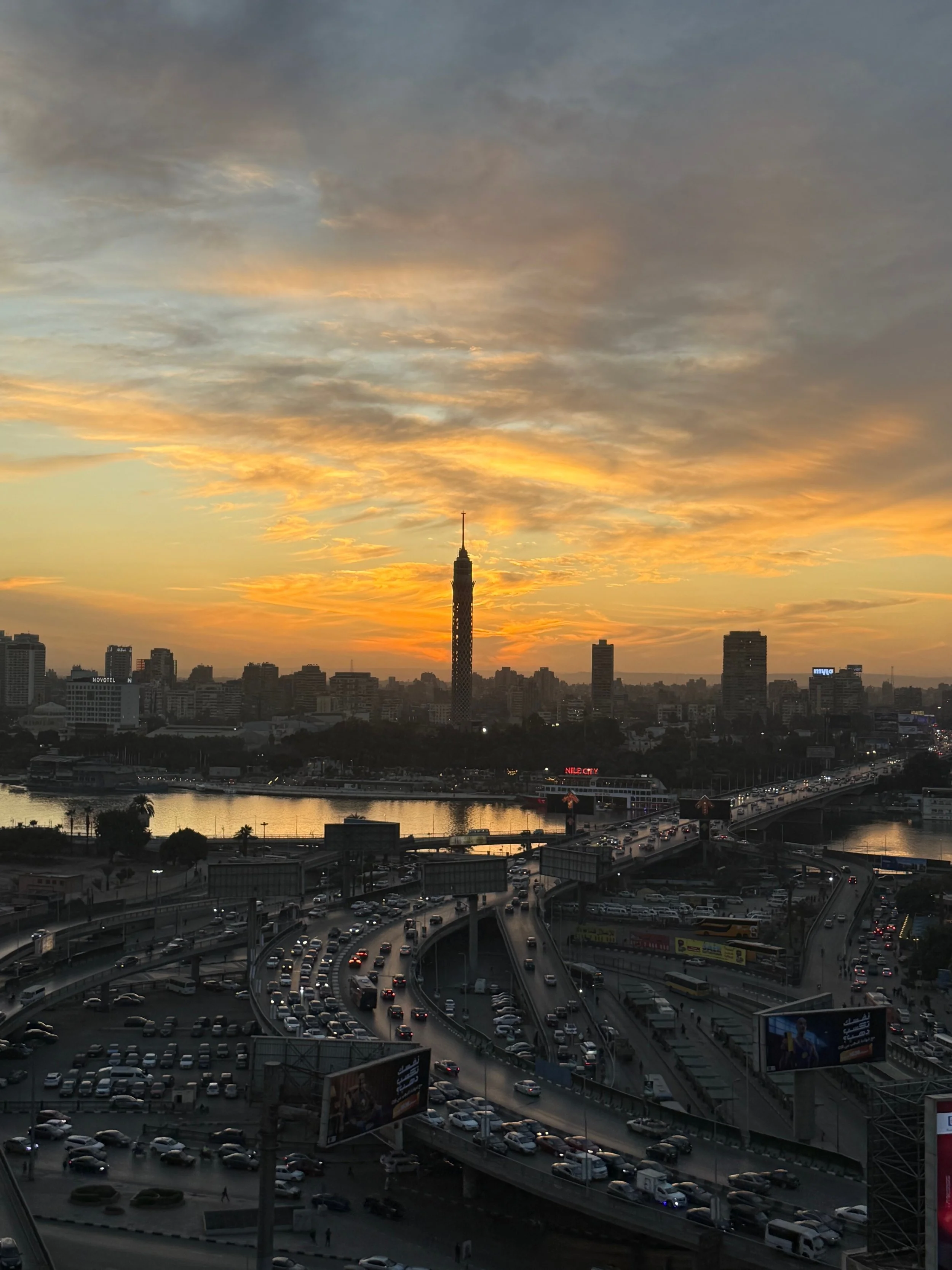 Rush-hour traffic flowing toward the Nile beneath the Cairo Tower at sunset.