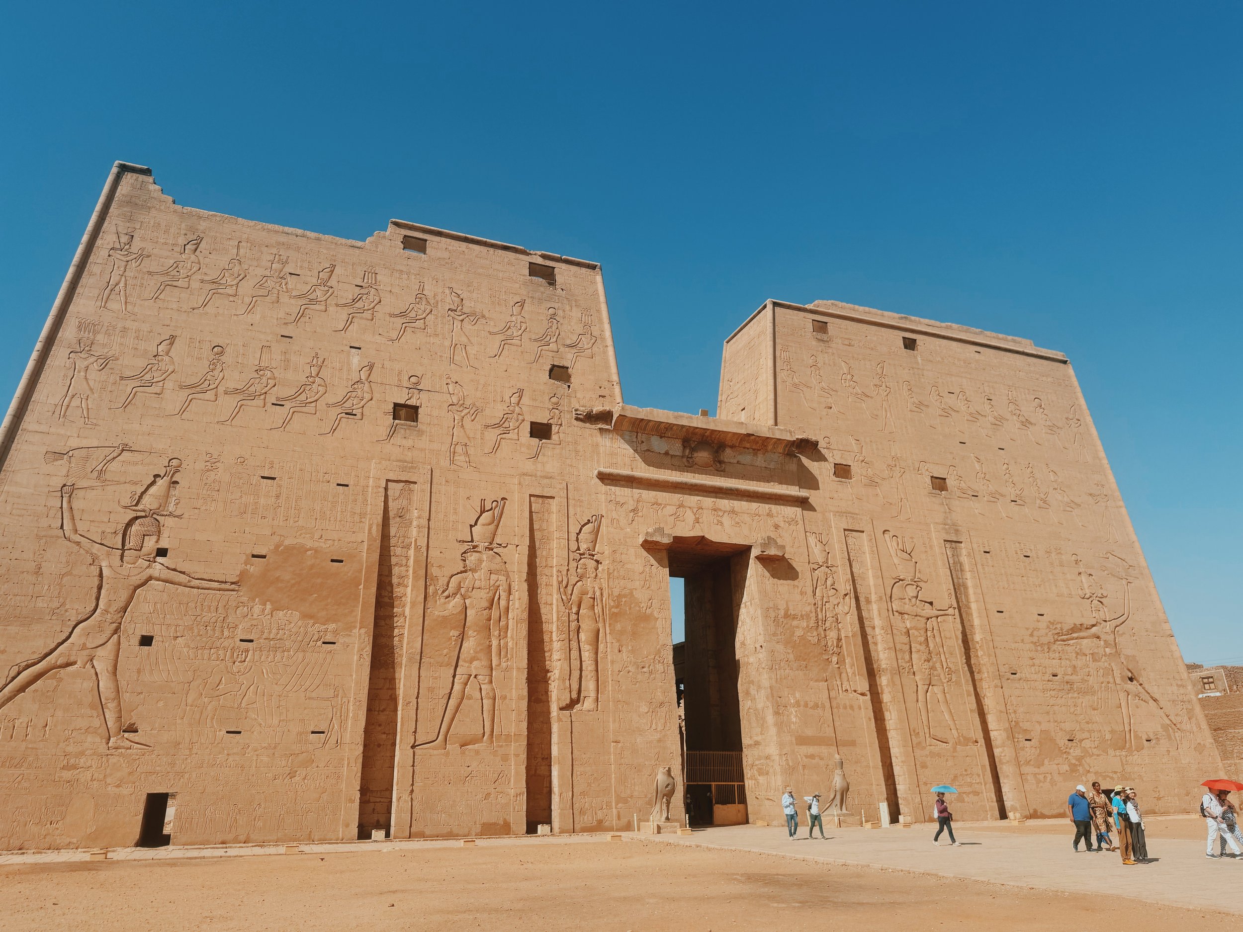 The towering carved first pylon of the Temple of Horus at Edfu, guarded by granite falcons.