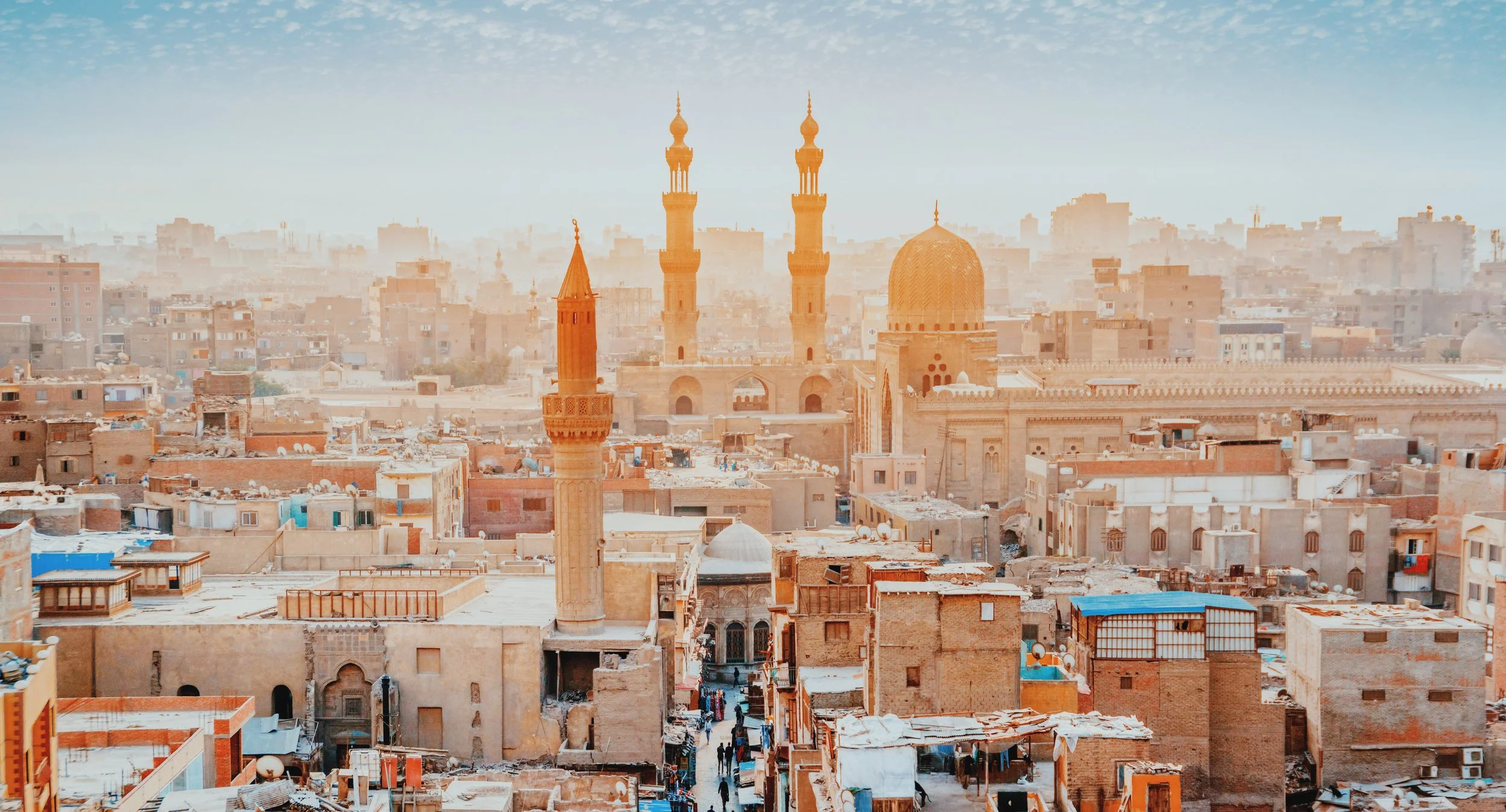 Minarets and domes rising above the rooftops of Islamic Cairo in hazy golden light