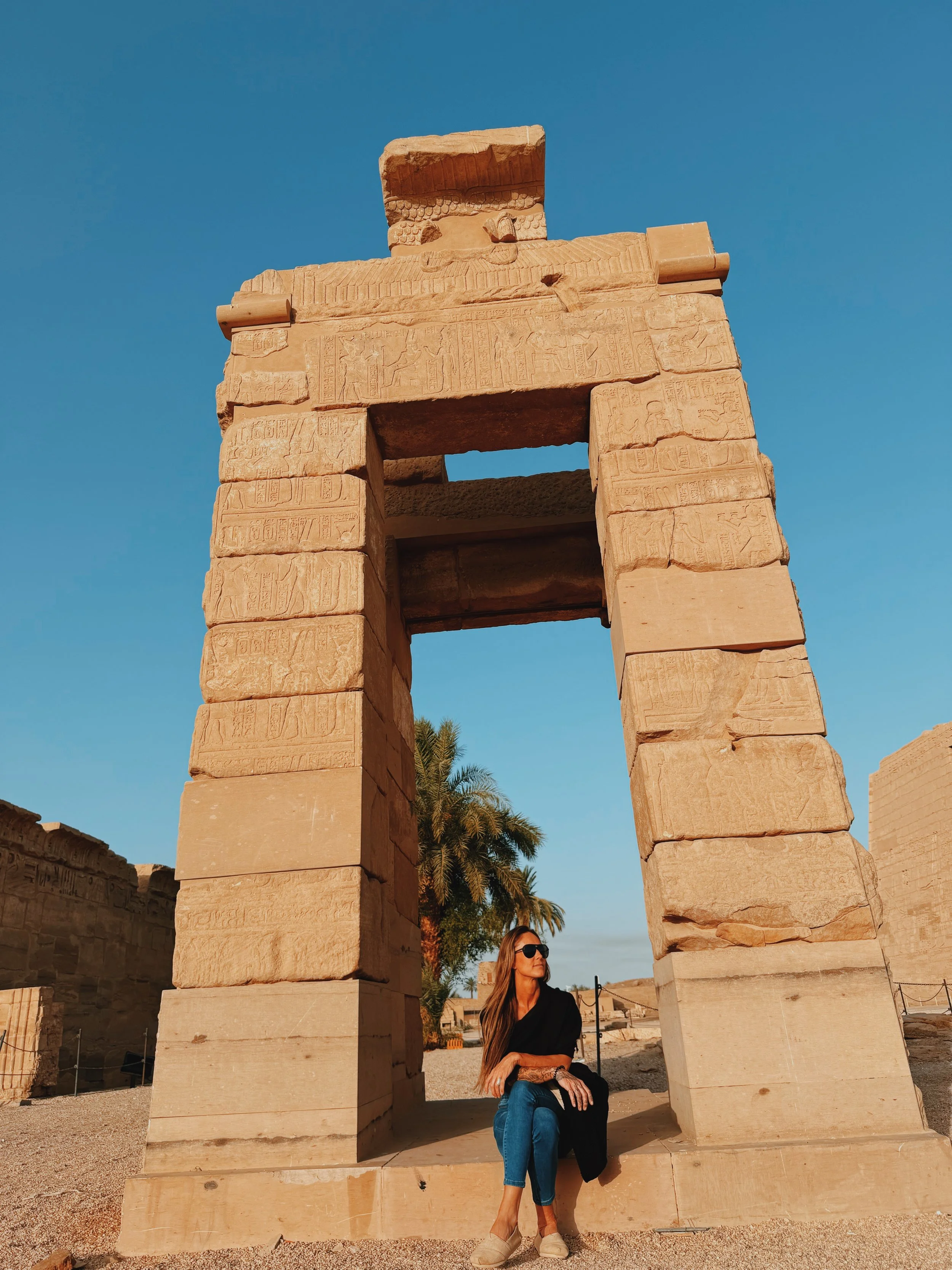 Jennifer of Takemet Tours sitting beneath an ancient carved gateway at Medinet Habu temple on Luxor’s West Bank in early morning light.