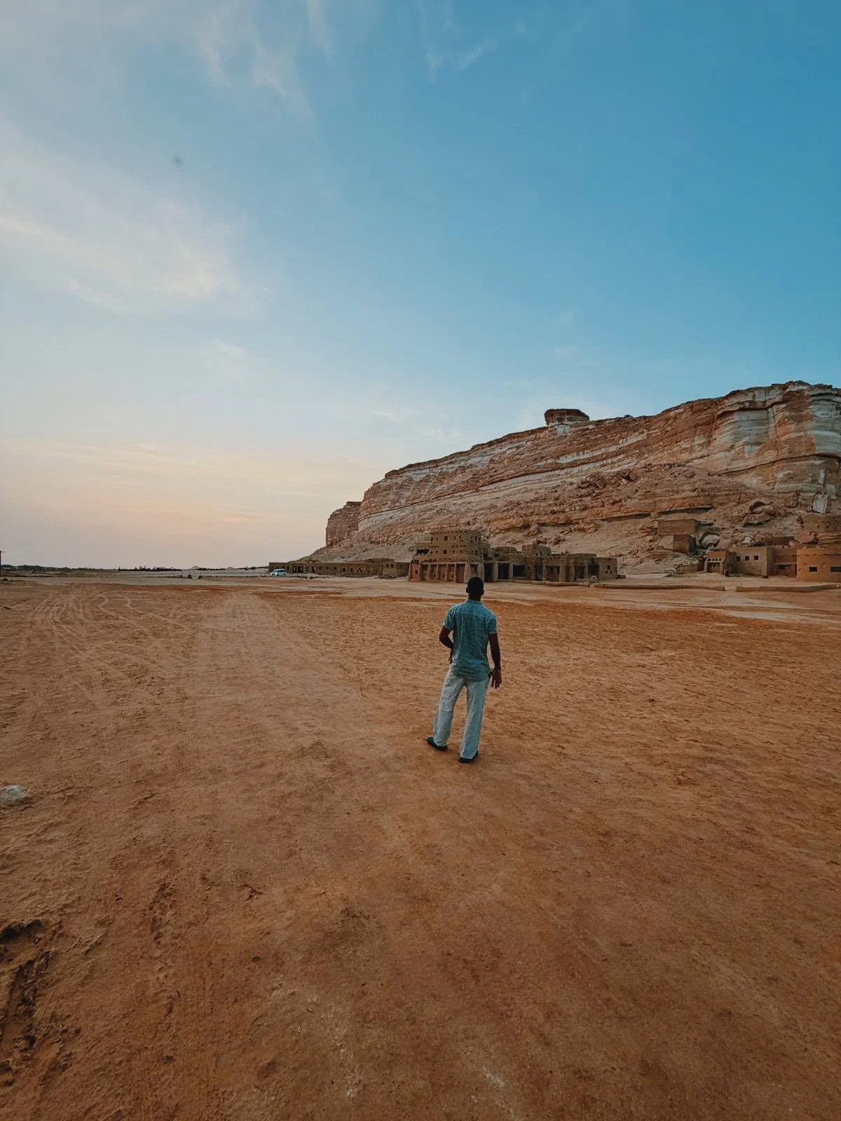 Mostafa walking across the desert toward the cliffs of Siwa Oasis at dusk.