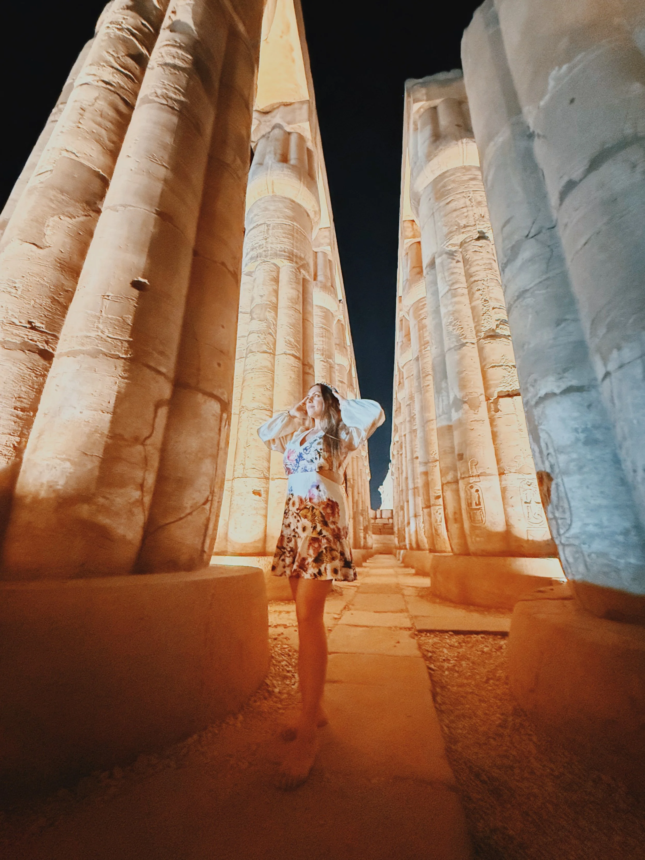 A traveler standing among the illuminated columns of Luxor Temple at night.