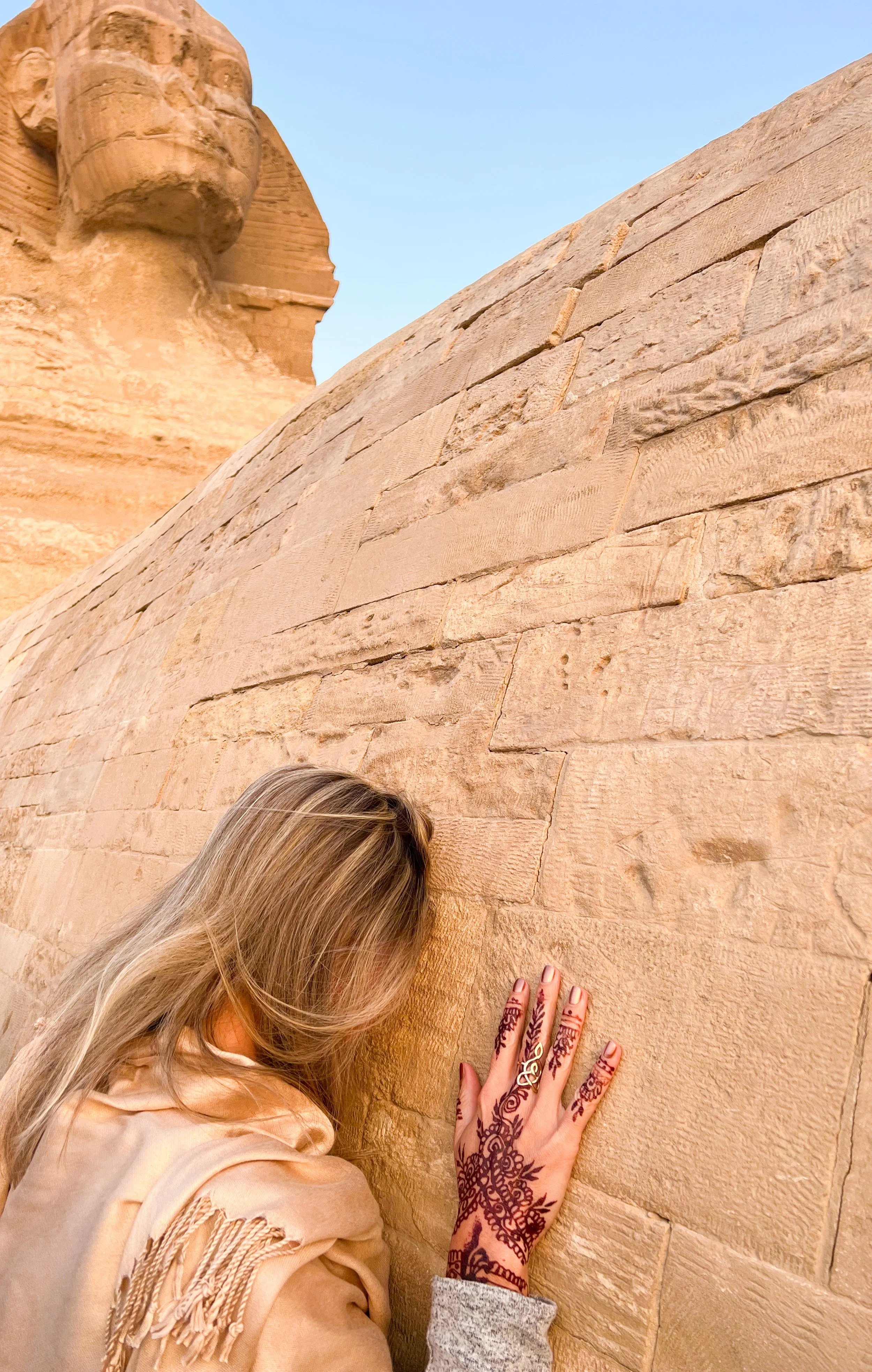 A traveler resting her forehead and hennaed hand against the ancient stones of the Great Sphinx of Giza in quiet reverence.