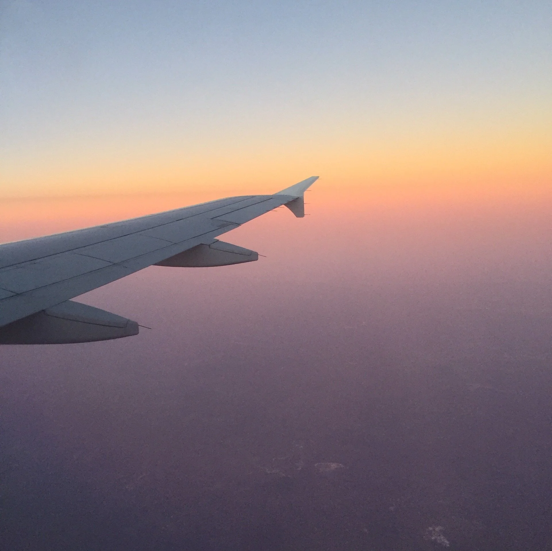 View from an airplane window of the wing silhouetted against a golden sunset sky as the journey home begins
