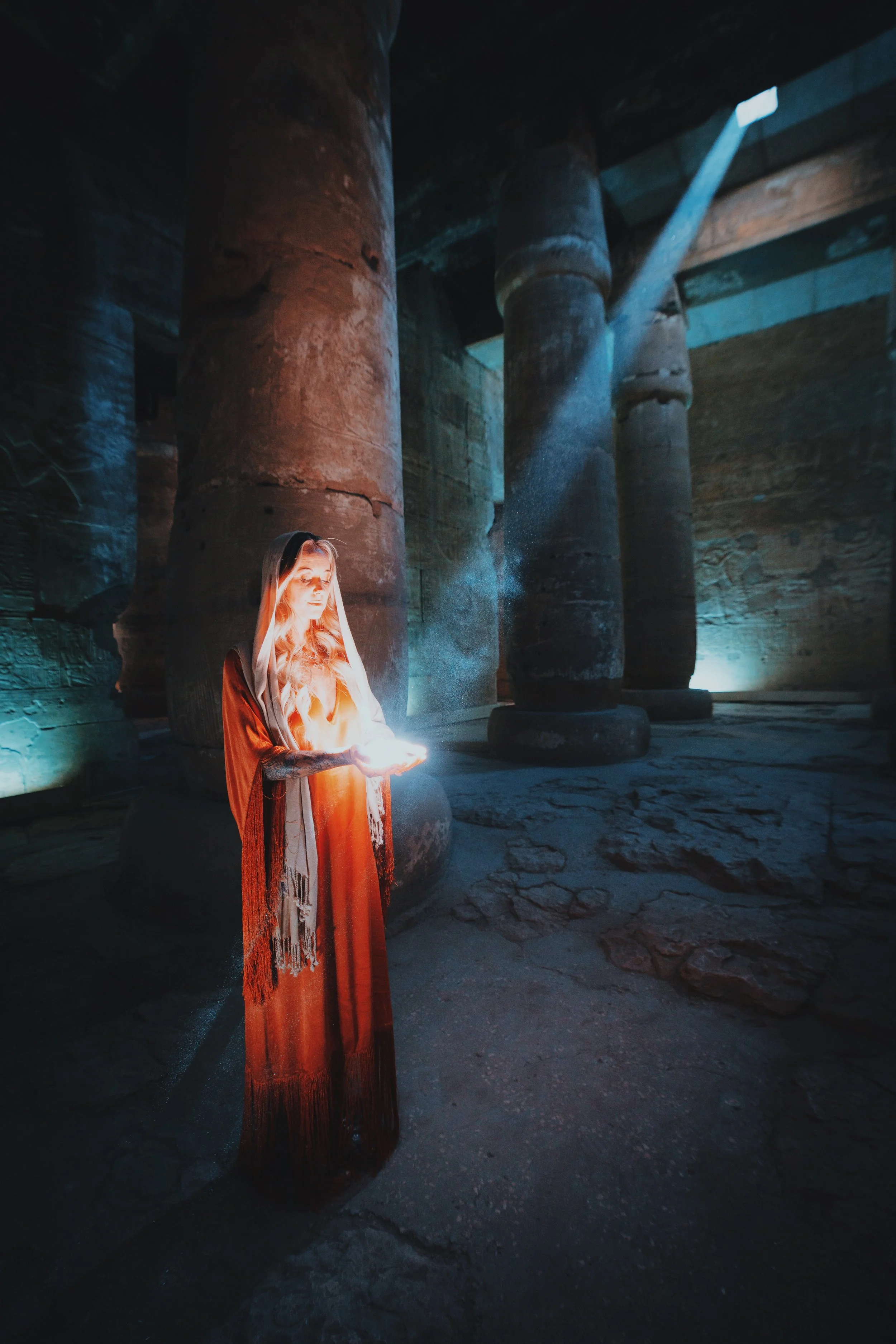 Veiled woman holding a glowing light in her cupped hands inside the dim hypostyle hall of the Temple of Seti I, Abydos