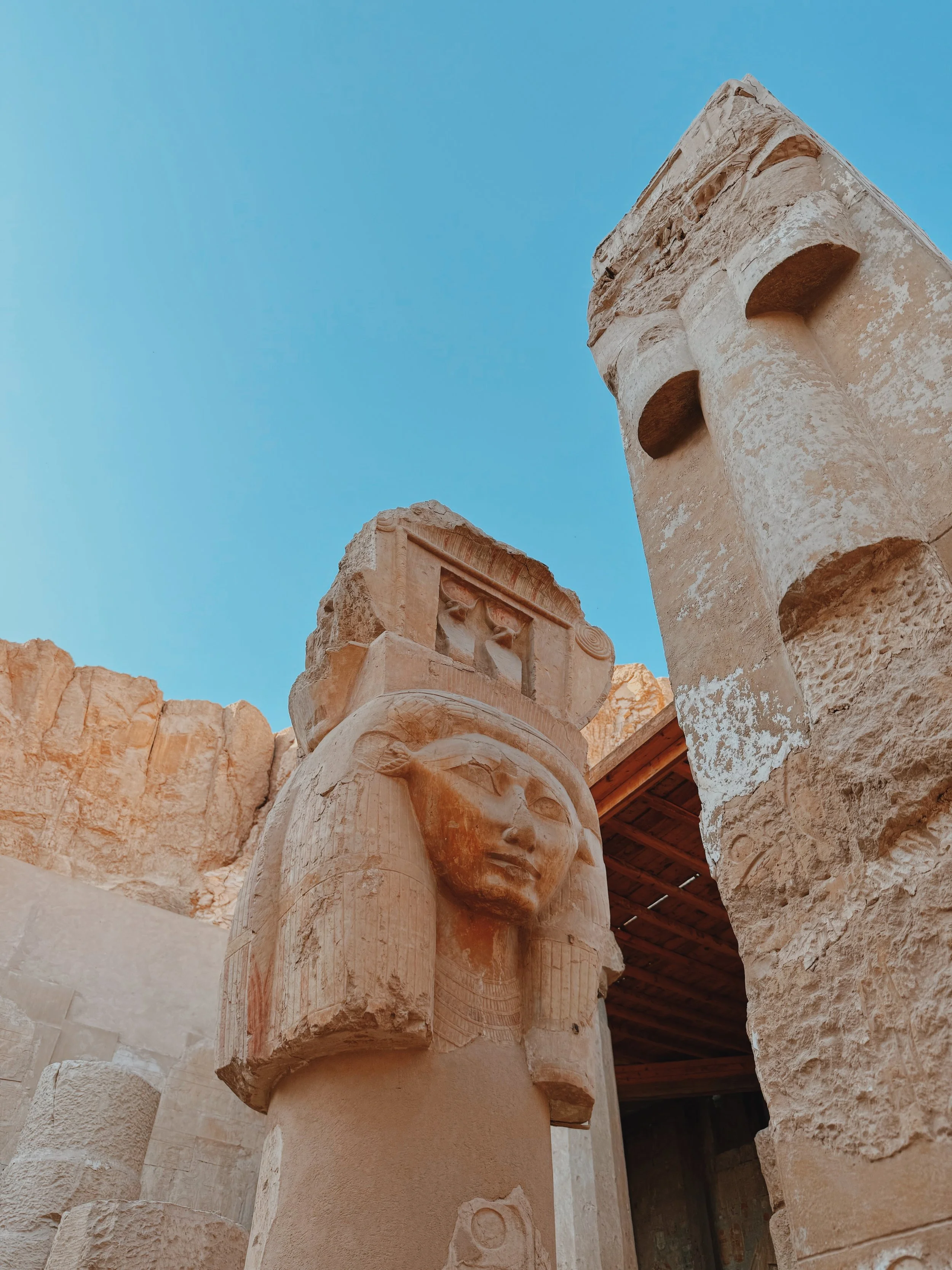 A carved Hathor-faced column at the Temple of Hatshepsut on Luxor's West Bank, with the golden cliffs of Deir el-Bahari behind