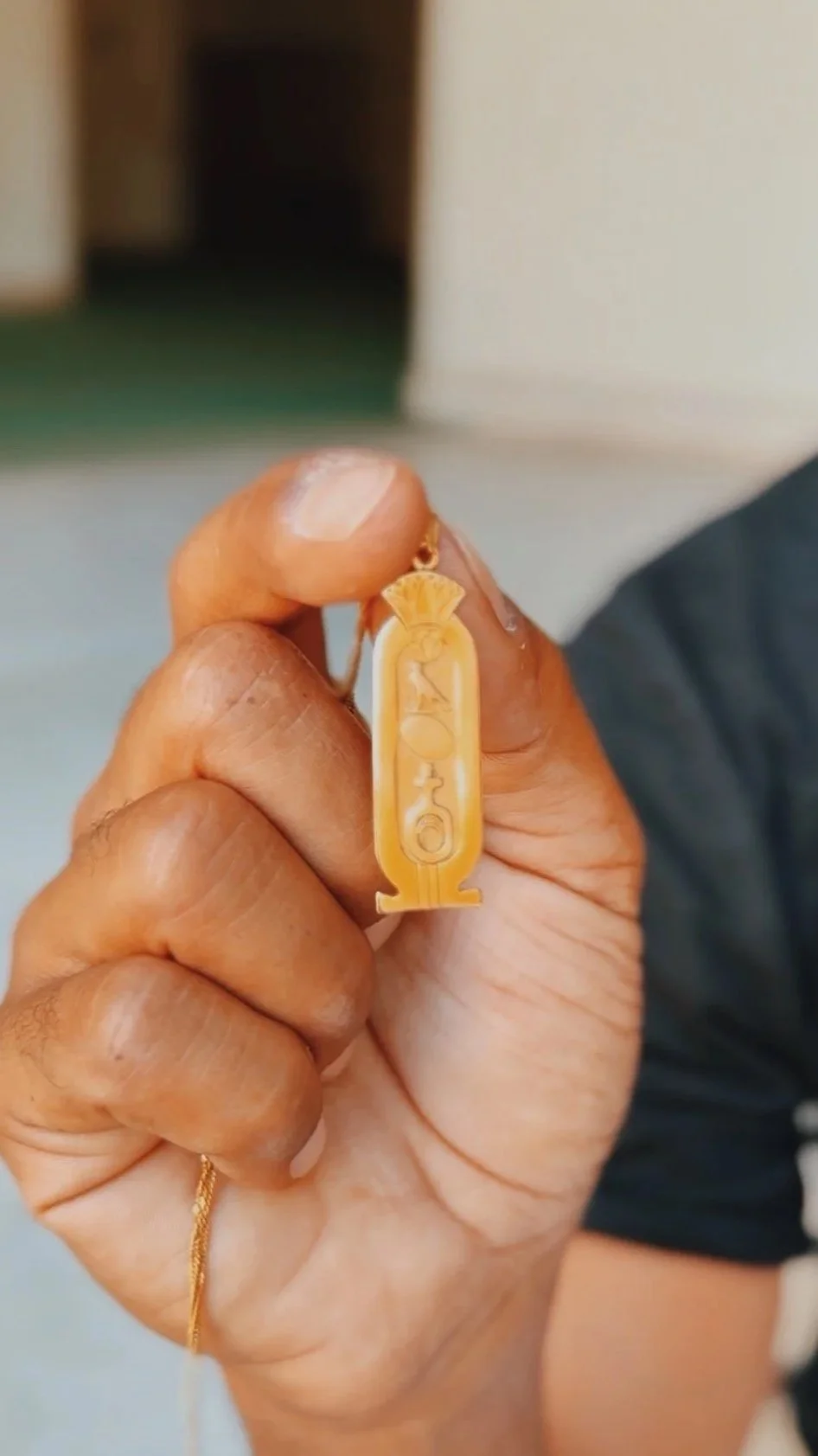 Mostafa holding a custom gold cartouche pendant engraved with hieroglyphs, crowned with a lotus