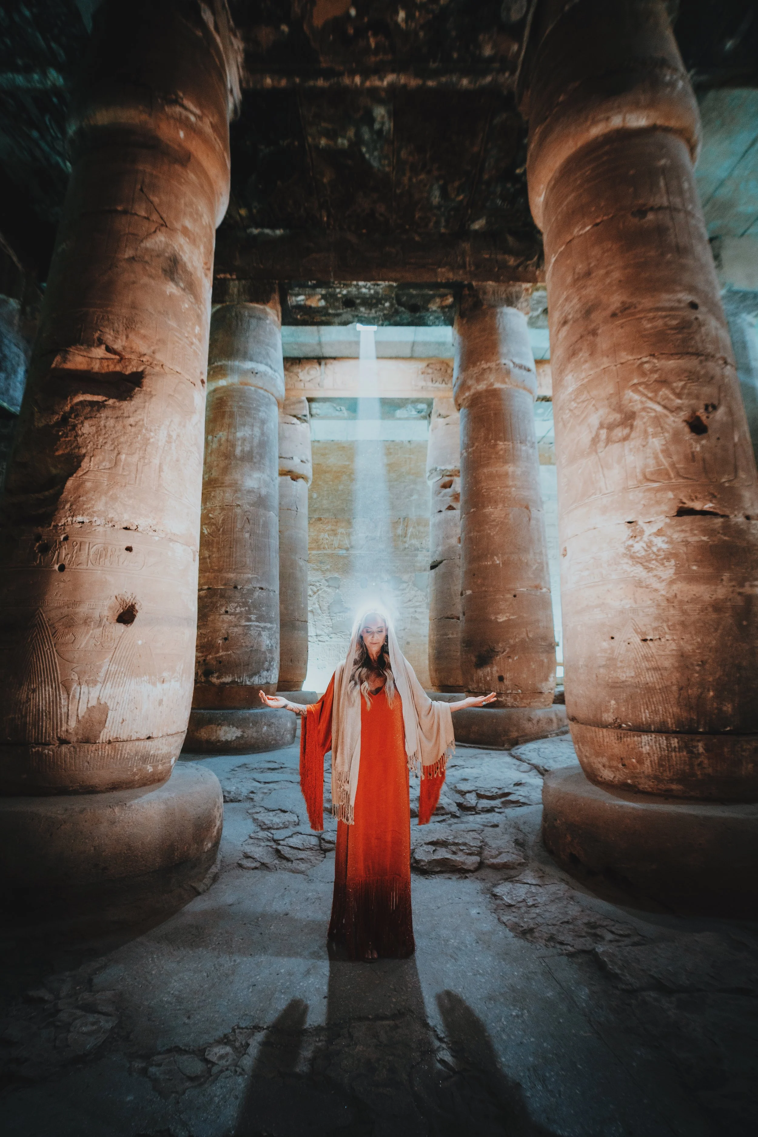Jennifer of Takemet Tours standing in a halo of light with open palms in the hypostyle hall of the Temple of Seti I, Abydos