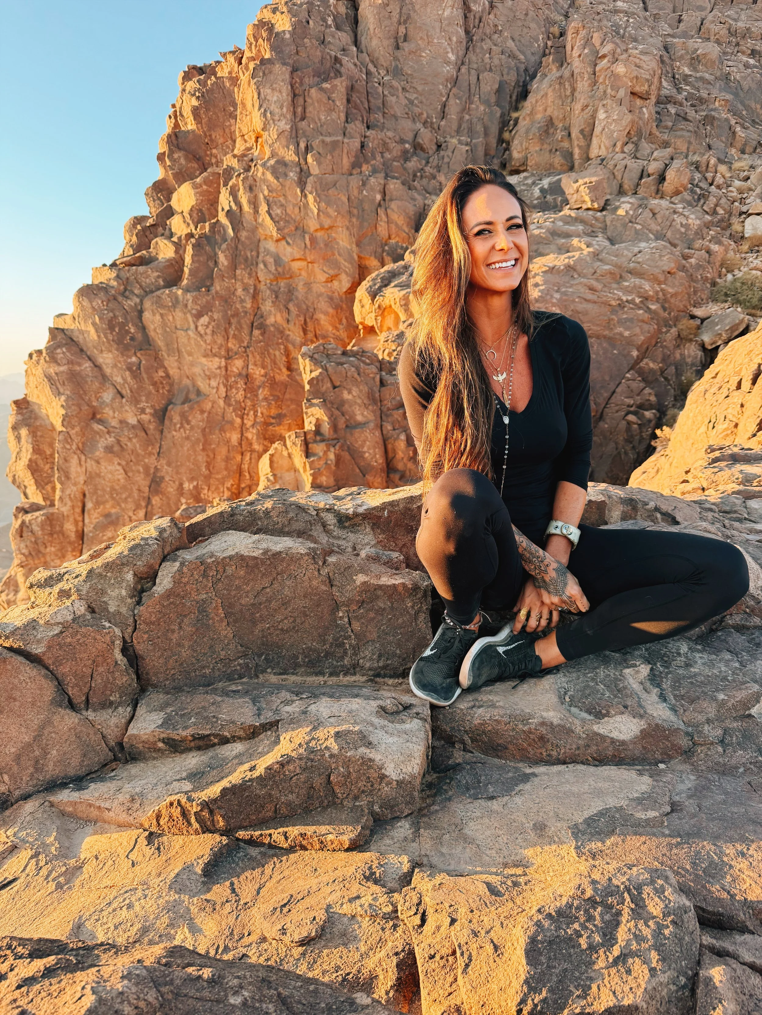 Jennifer of Takemet Tours smiling on the rocky summit of Mount Sinai in golden sunrise light