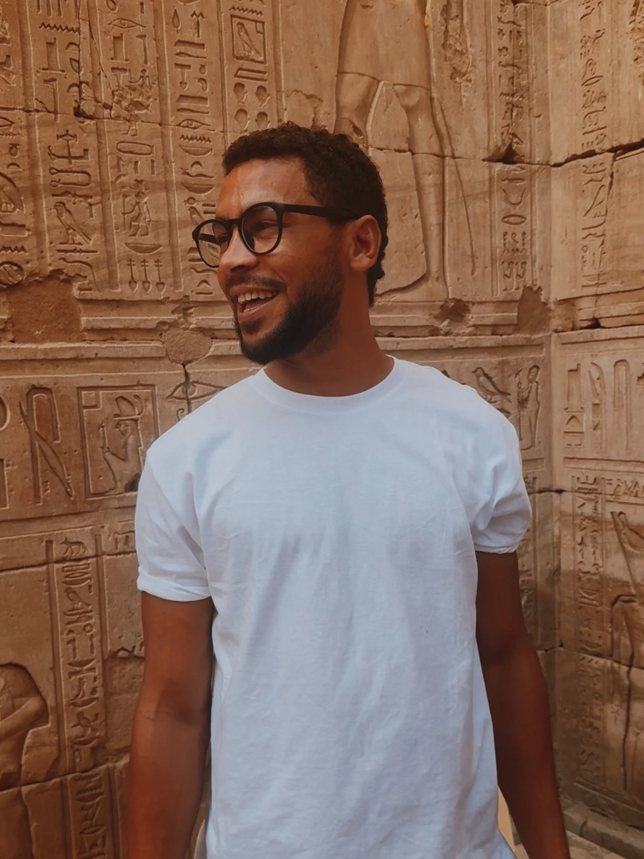 Egyptologist Mostafa of Takemet Tours smiling in front of a temple wall carved with hieroglyphs at Edfu