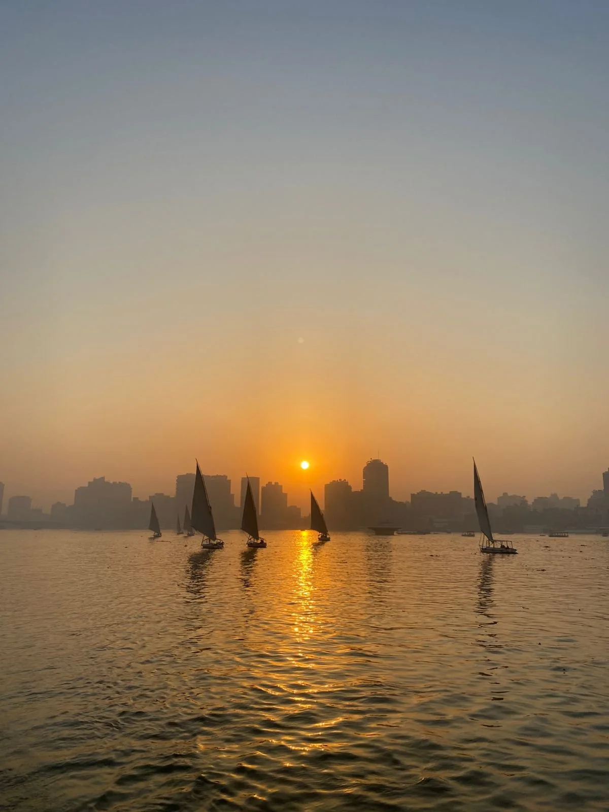 Traditional felucca sailboats on the Nile at sunset, with the Cairo skyline silhouetted against a golden sky