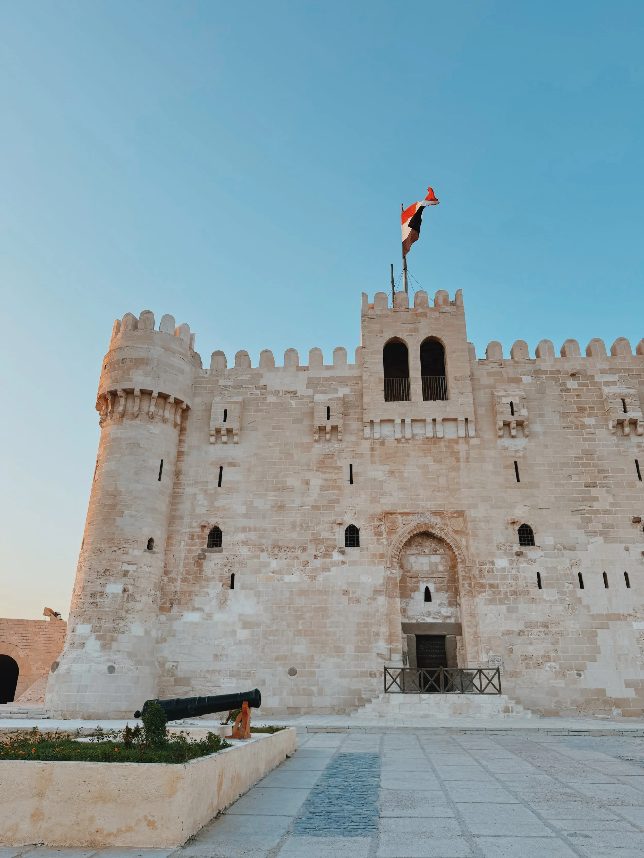 The Citadel of Qaitbay in Alexandria at golden hour, with an old cannon in the foreground.