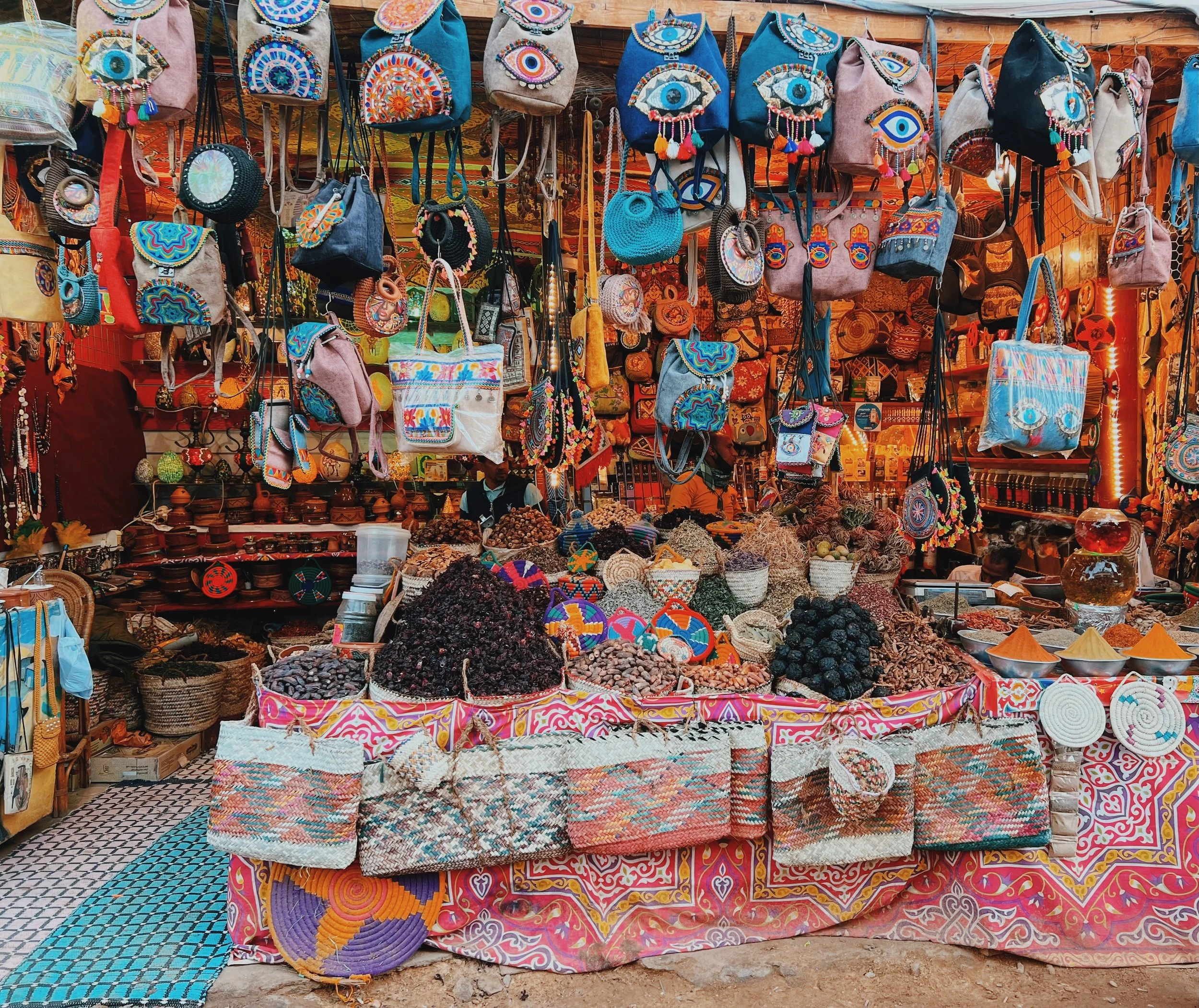 A Nubian village market stall piled with spices, dried hibiscus and dates, woven baskets and colorful embroidered bags