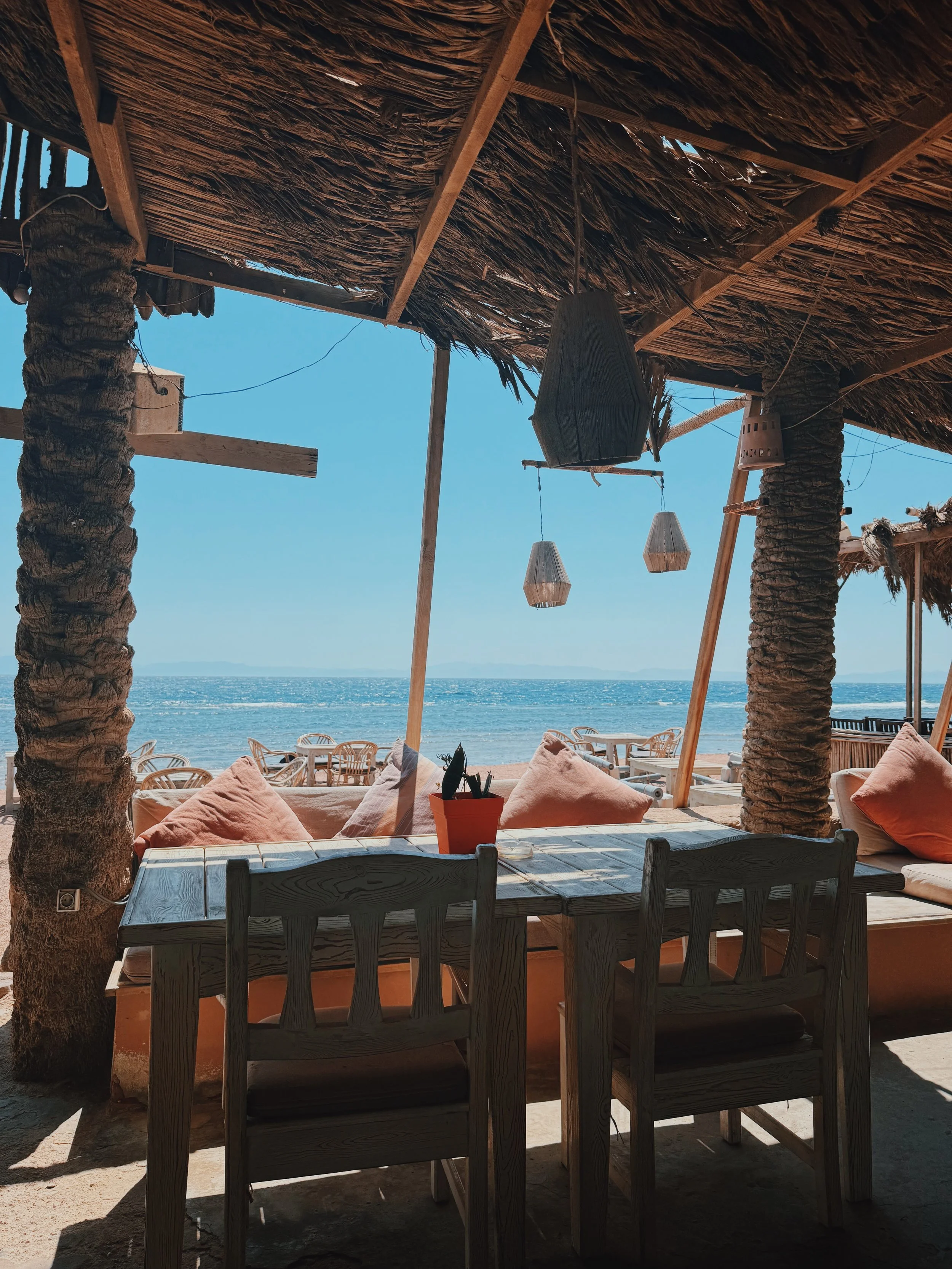 A shaded beach café with orange cushions and woven lanterns looking out over the Red Sea in Dahab.